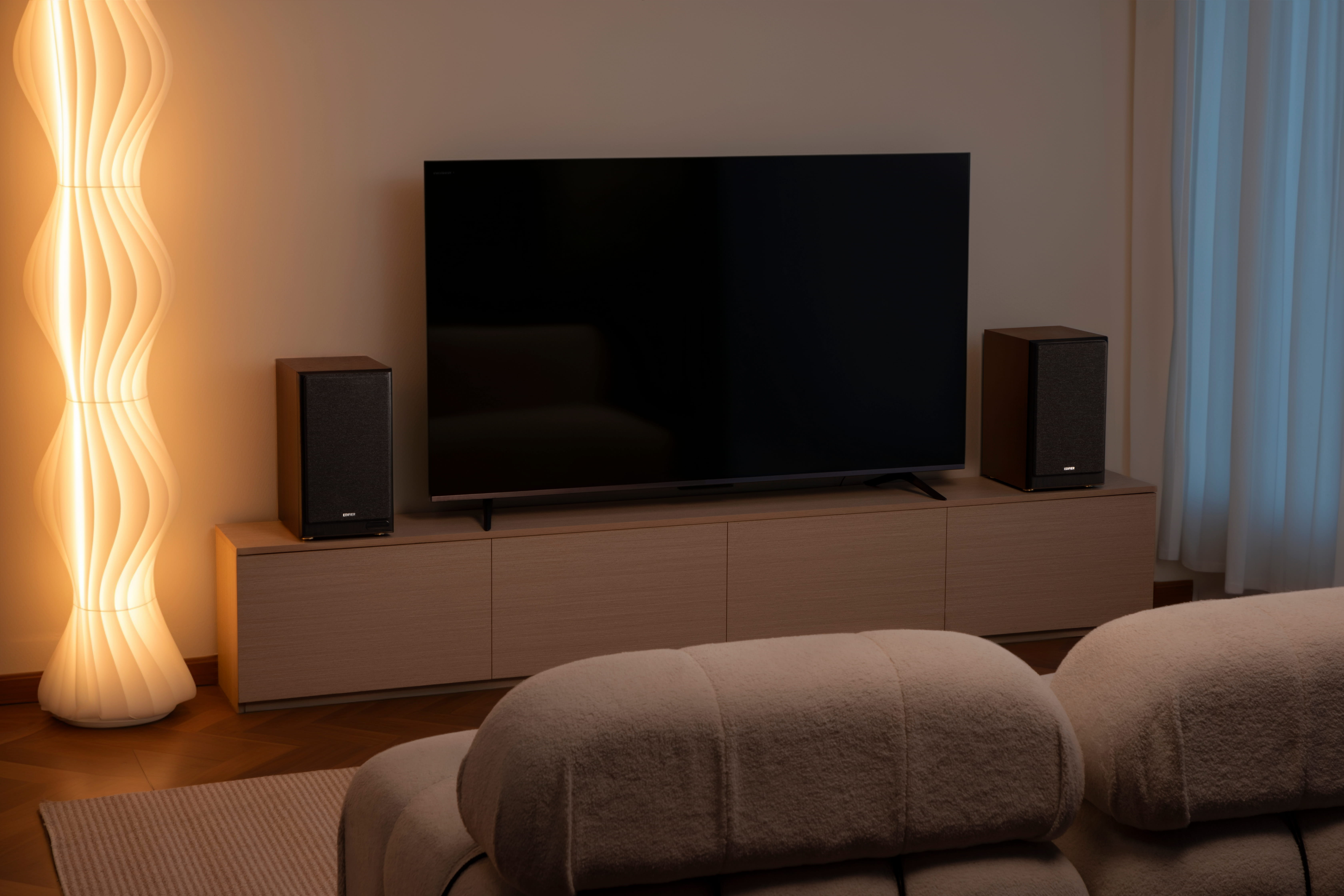 Ein Wohnzimmer mit Fernseher, Lautsprechern, Lampe und Sofa.