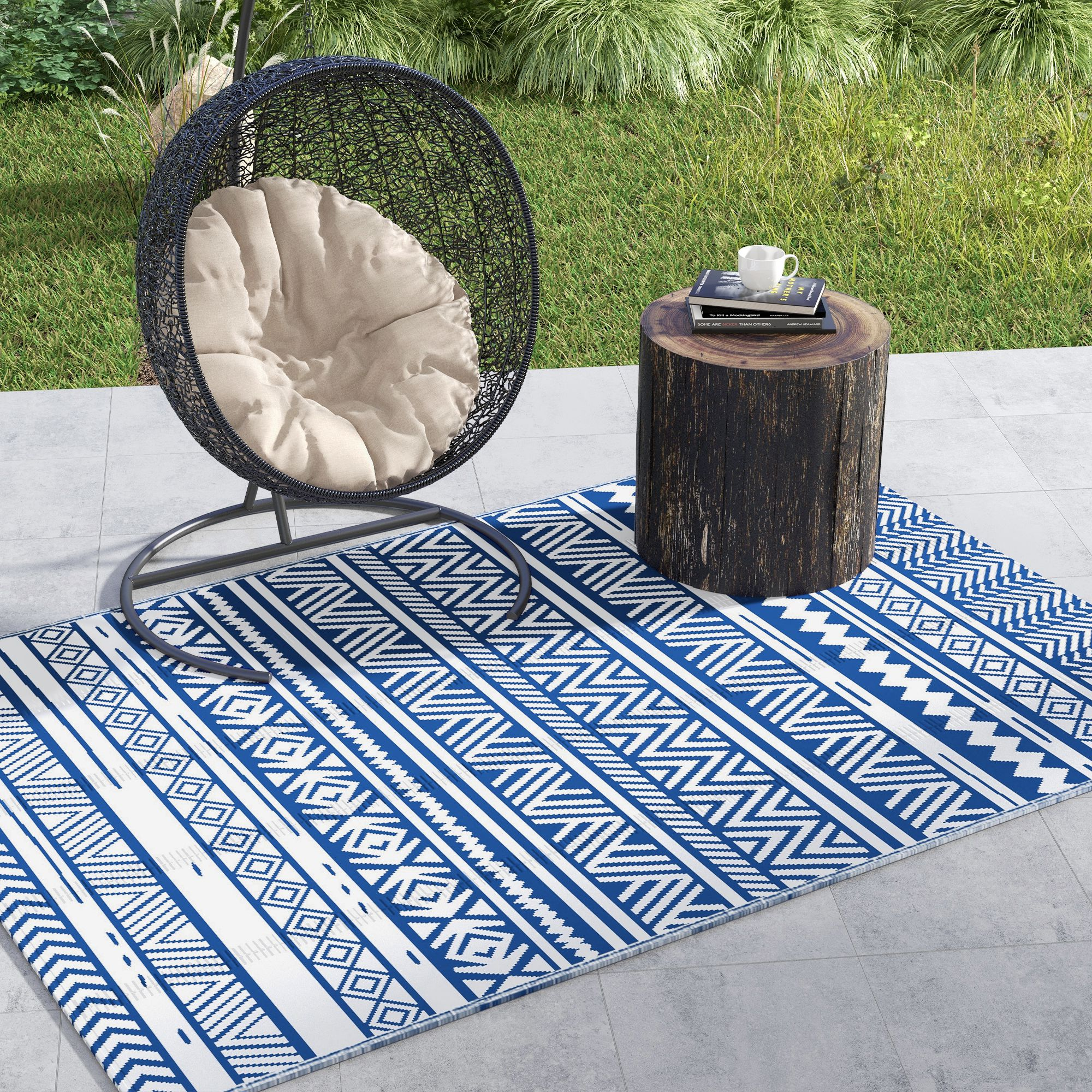 Una silla de cesta colgante negra con cojín beige se asienta sobre una alfombra azul y blanca.