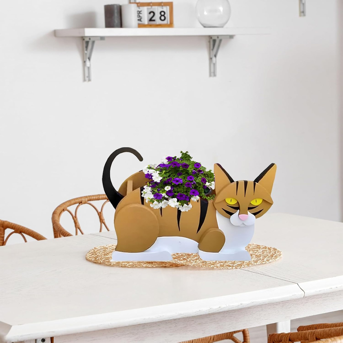 Ein Katzen-Blumentopf mit lila und weißen Blumen auf einem Tisch.