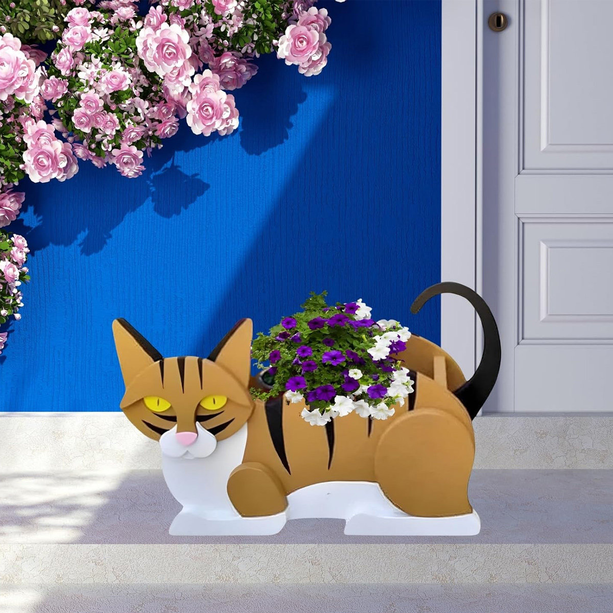 Eine Katzen-Blumenampel mit lila und weißen Blumen vor einer blauen Wand.
