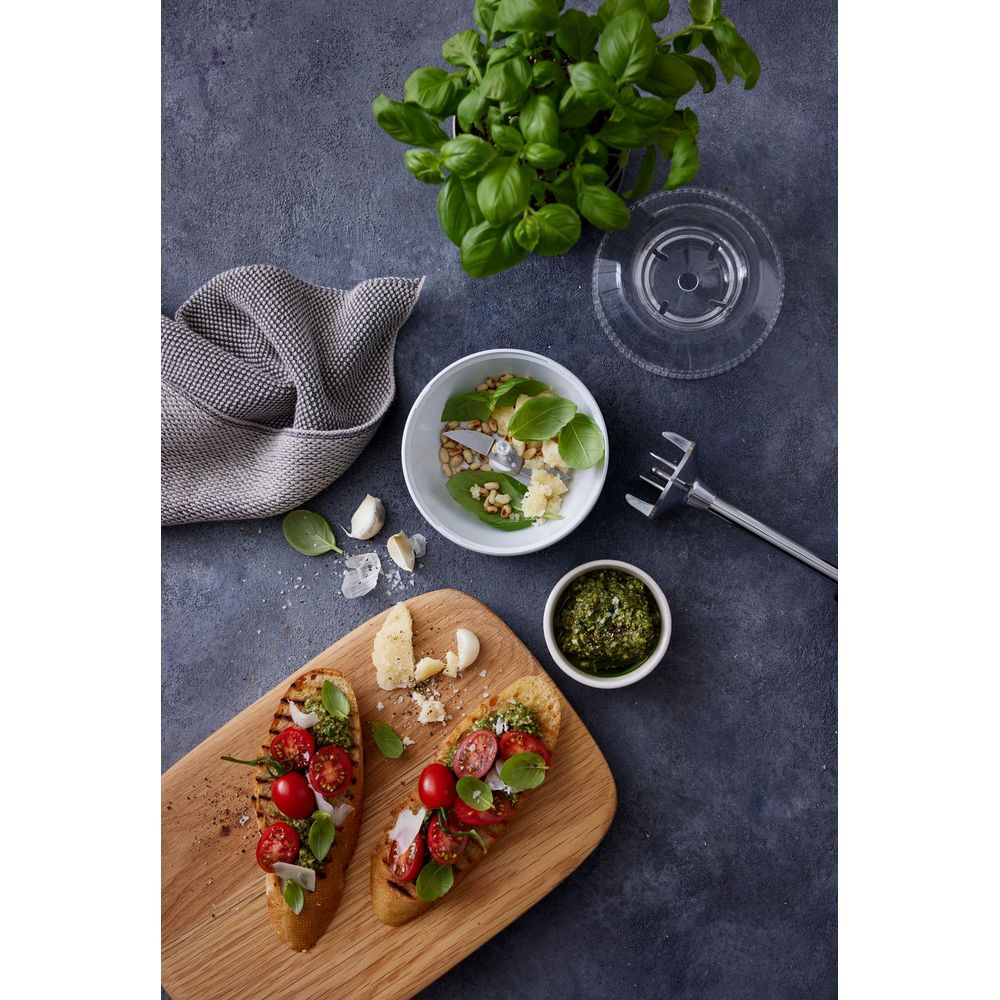 Bruschetta mit Tomaten und Basilikum, daneben Zutaten für Pesto auf einem Holztisch.