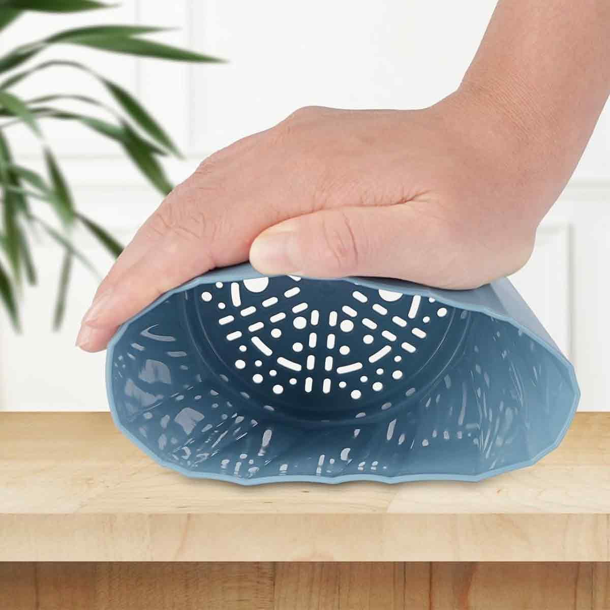 Eine Hand drückt auf einen blauen Siebkorb mit Löchern auf einem Holztisch.