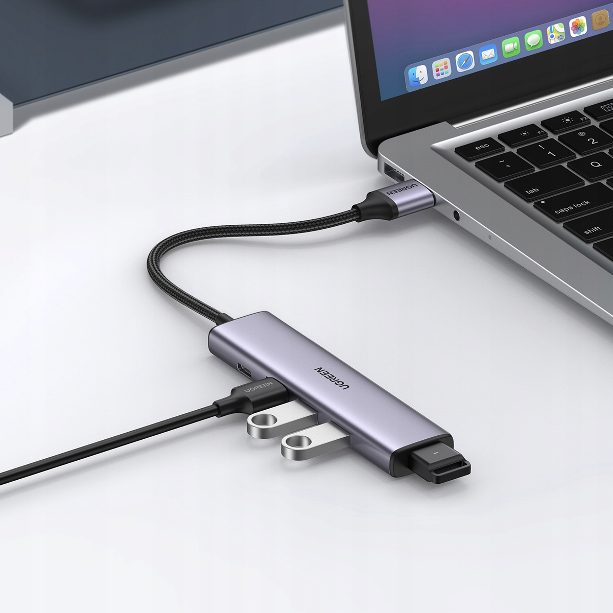 Srebrny hub USB-C jest podłączony do laptopa, z wpiętymi pendrive'ami.