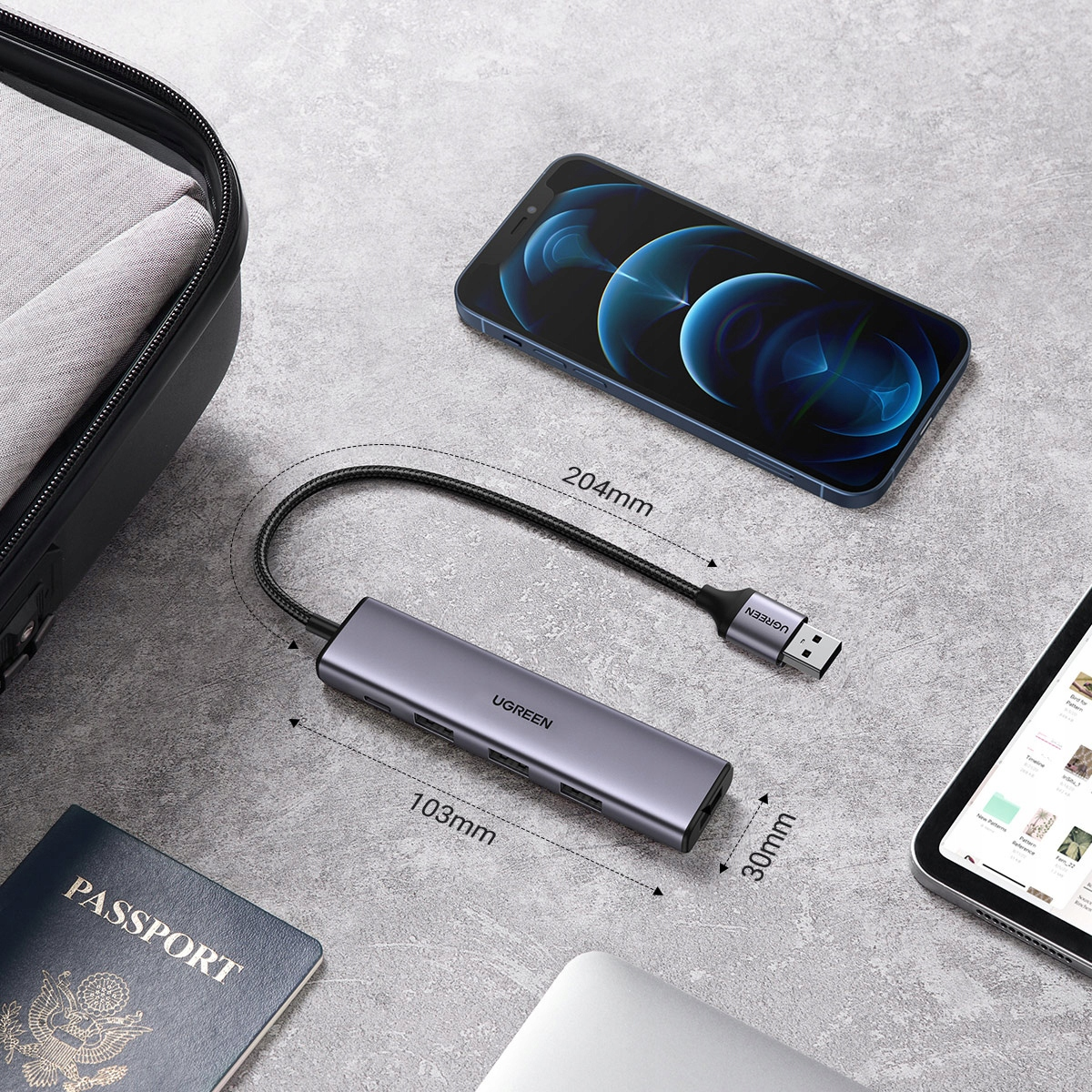 Szary hub USB z portami, połączony kablem z USB-A. Obok telefonu, paszportu, torby, tabletu.