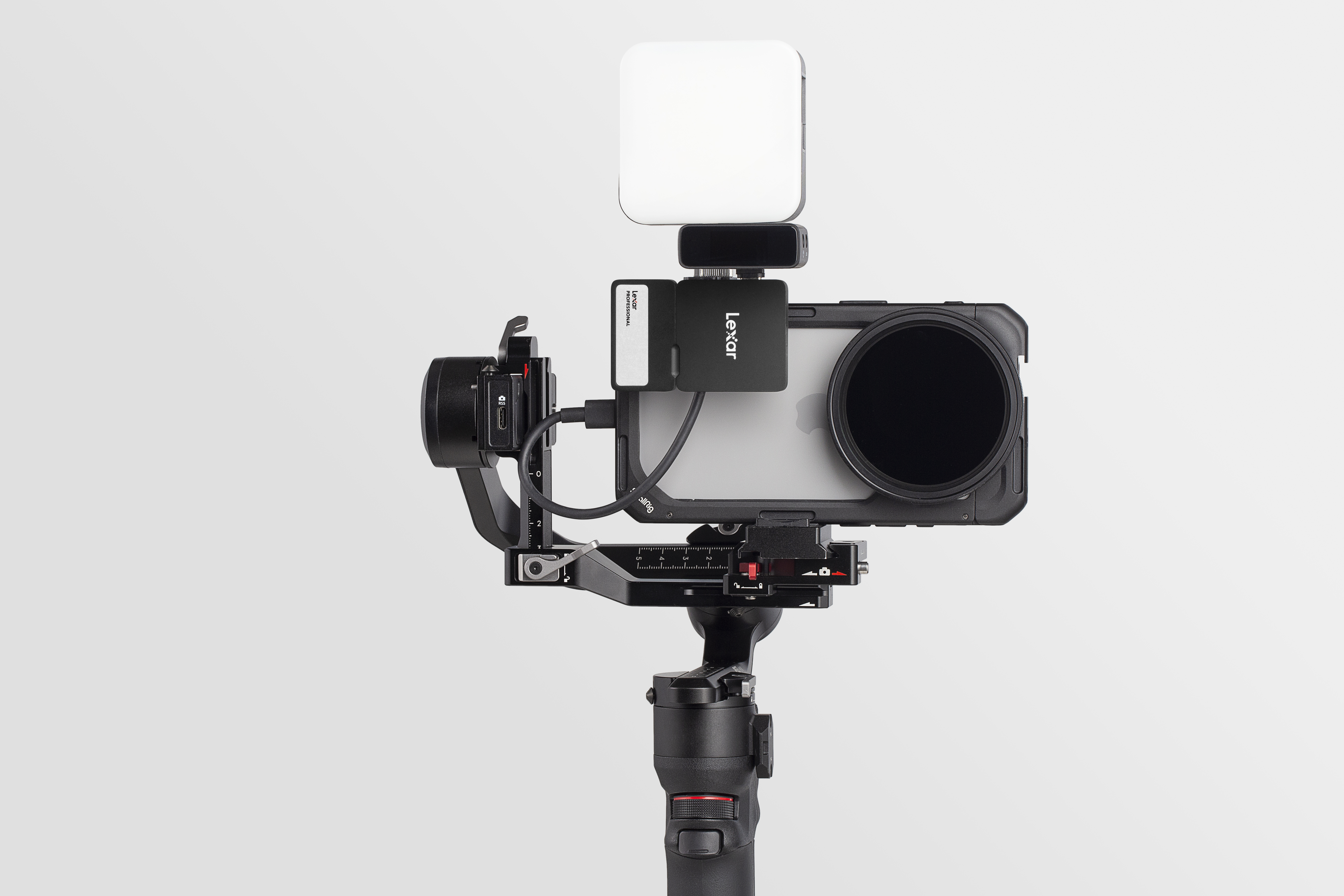 Un smartphone en un gimbal con luz y filtro, sobre fondo claro.