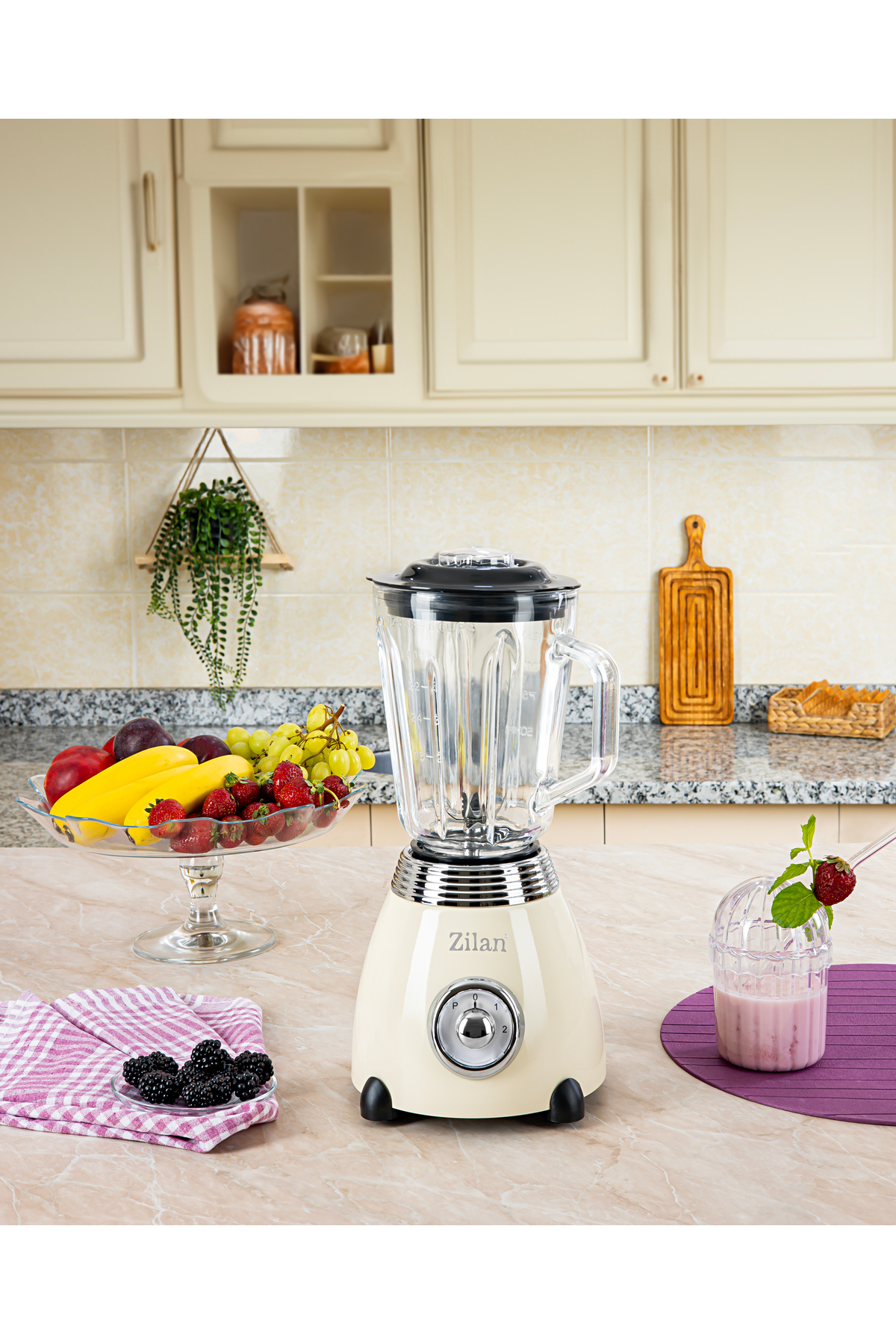 Krem rengi blender, meyve kasesi ve smoothie yanında mermer tezgahta duruyor.