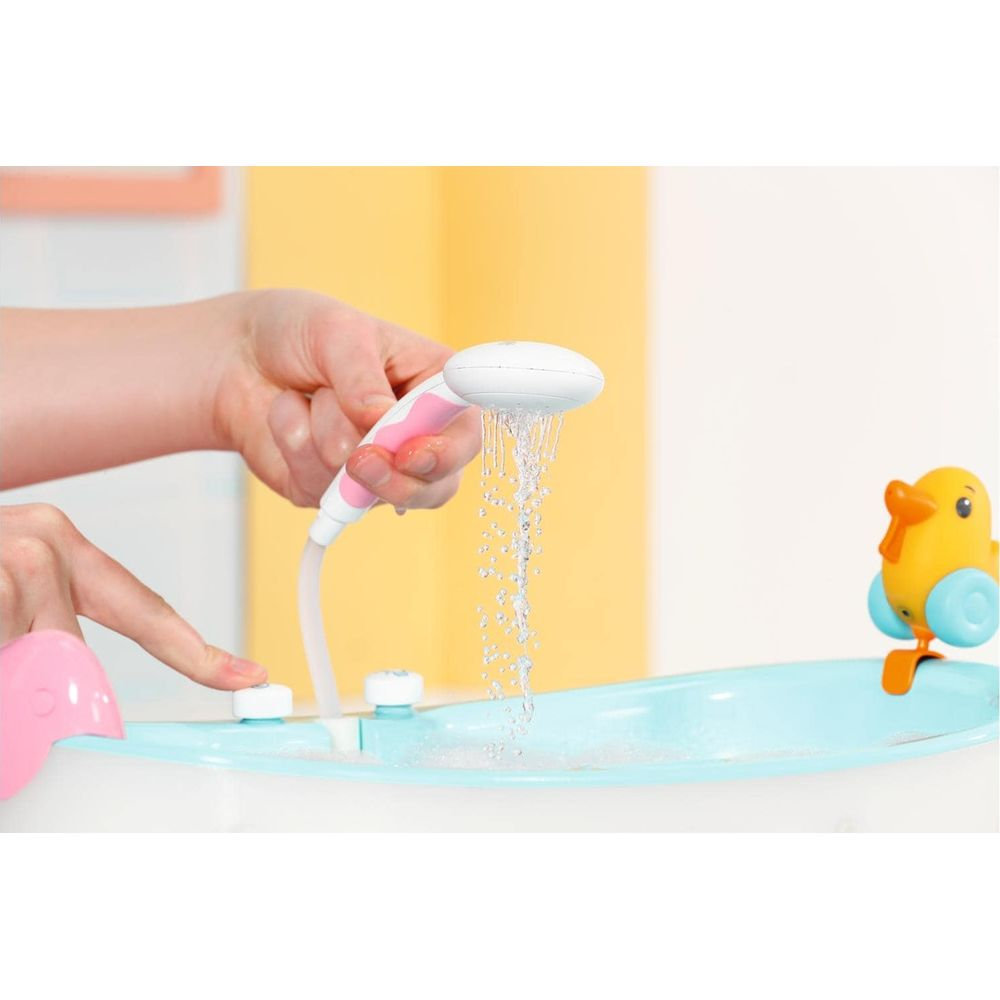Una mano sostiene una alcachofa de ducha rosa y blanca sobre una bañera de bebé azul. Agua fluye.