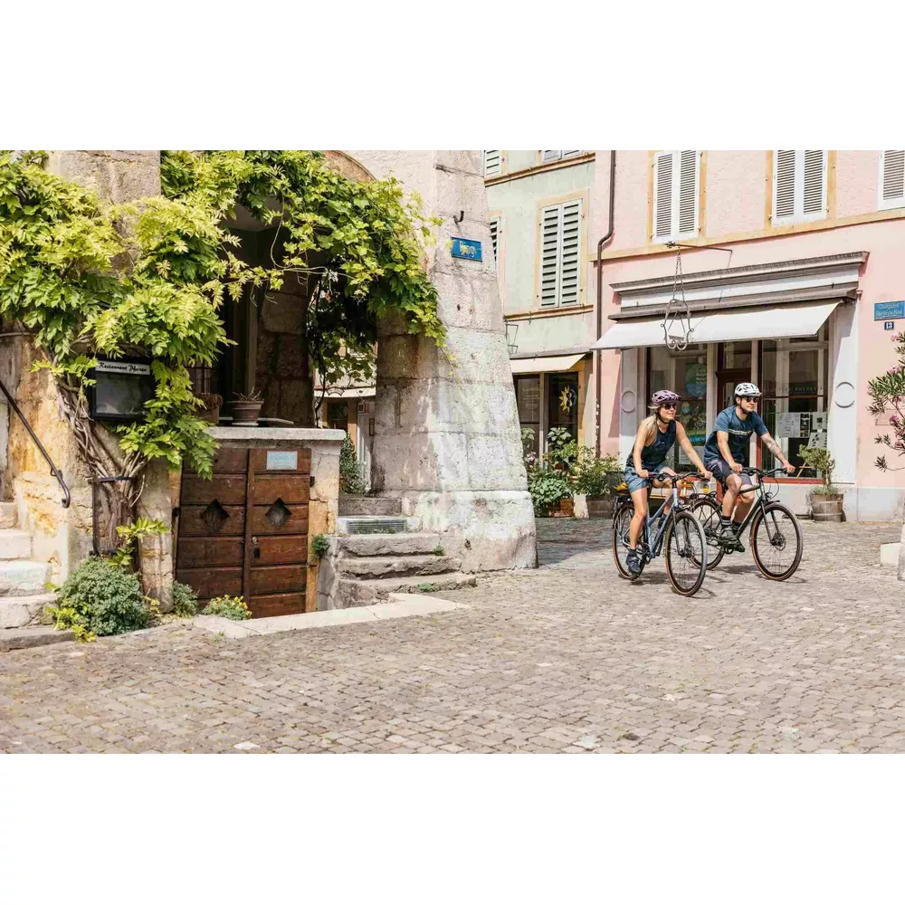 Ein Mann und eine Frau fahren Fahrrad auf einer Kopfsteinpflasterstraße vor alten Gebäuden.