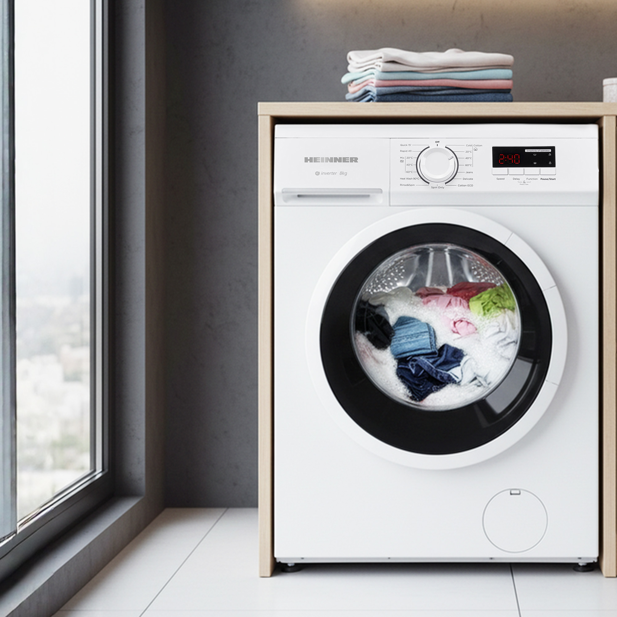 A white washing machine with a full load of colorful laundry and suds is shown in a modern room with a window.