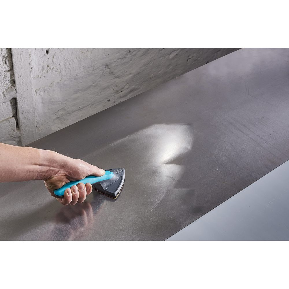 Une main tient un bloc de ponçage à manche bleu pour polir une surface métallique.