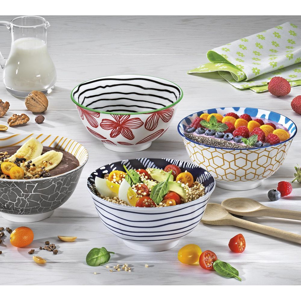 Quattro ciotole con frutta e cereali, accanto a una caraffa di latte e noci.