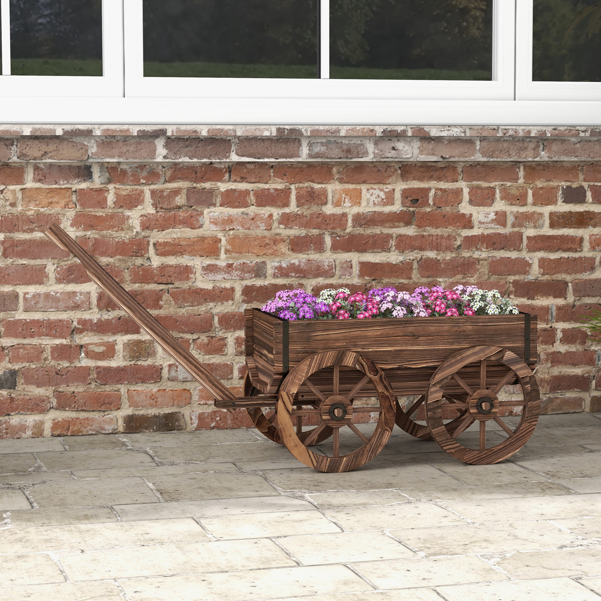 Ein hölzerner Wagen mit bunten Blumen steht auf einem gepflasterten Weg vor einer Ziegelwand.