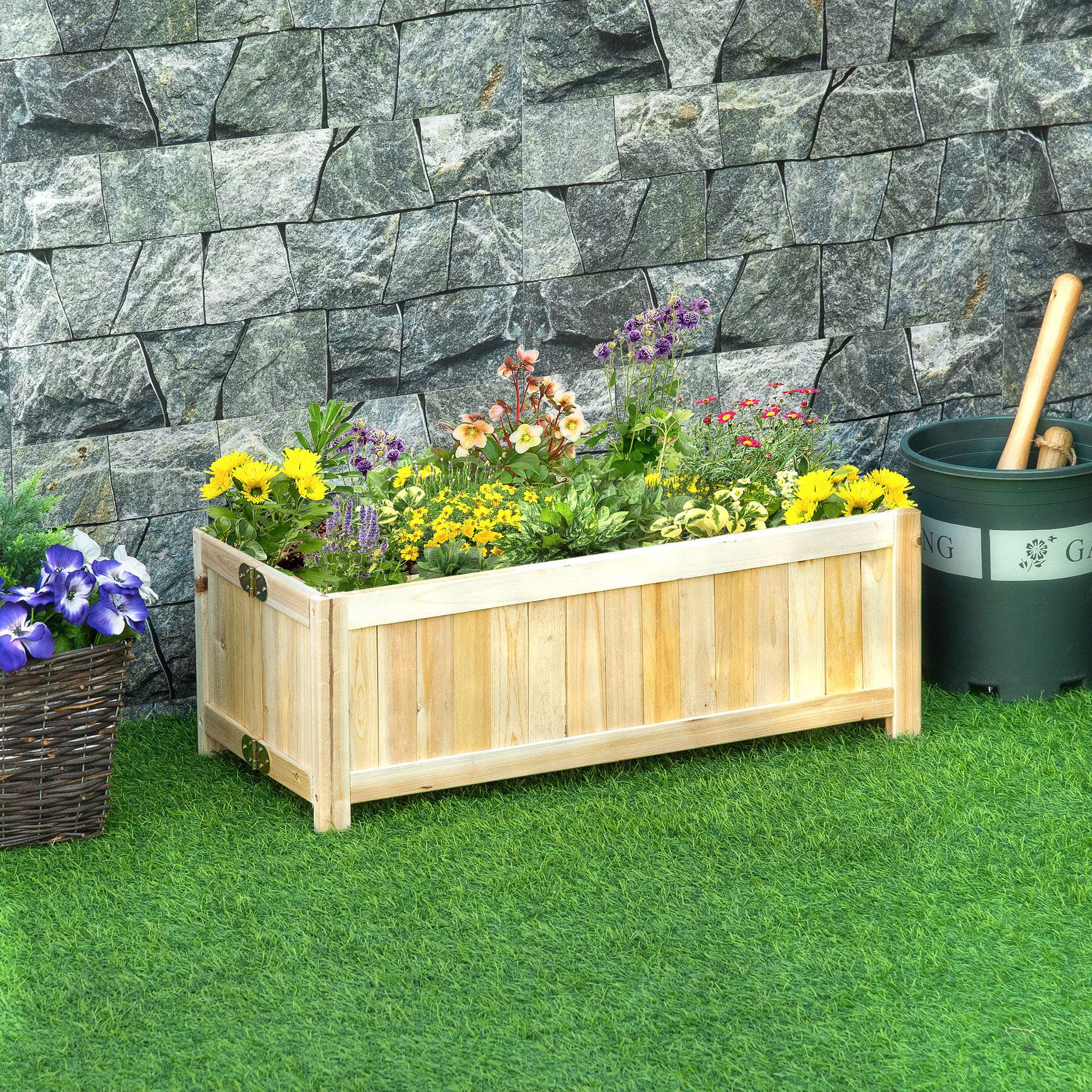Ein hölzerner Pflanztrog voller bunter Blumen vor einer Steinmauer.