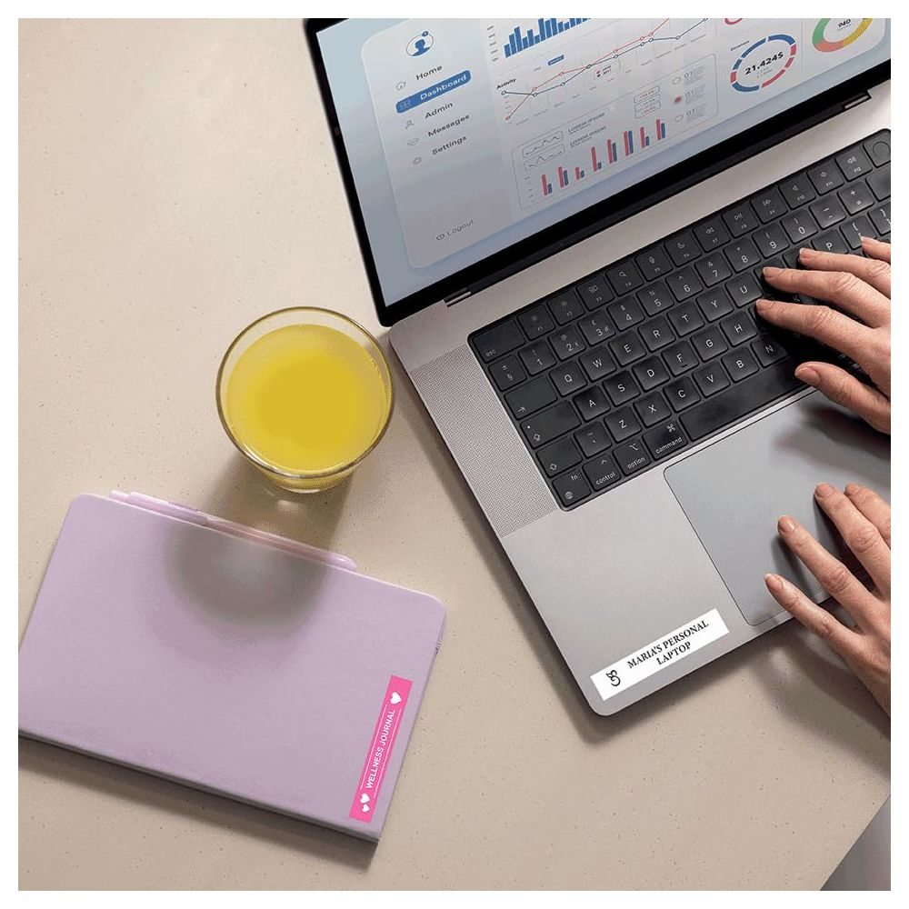 Laptop z wykresami, szklanka soku i fioletowy notatnik na biurku.