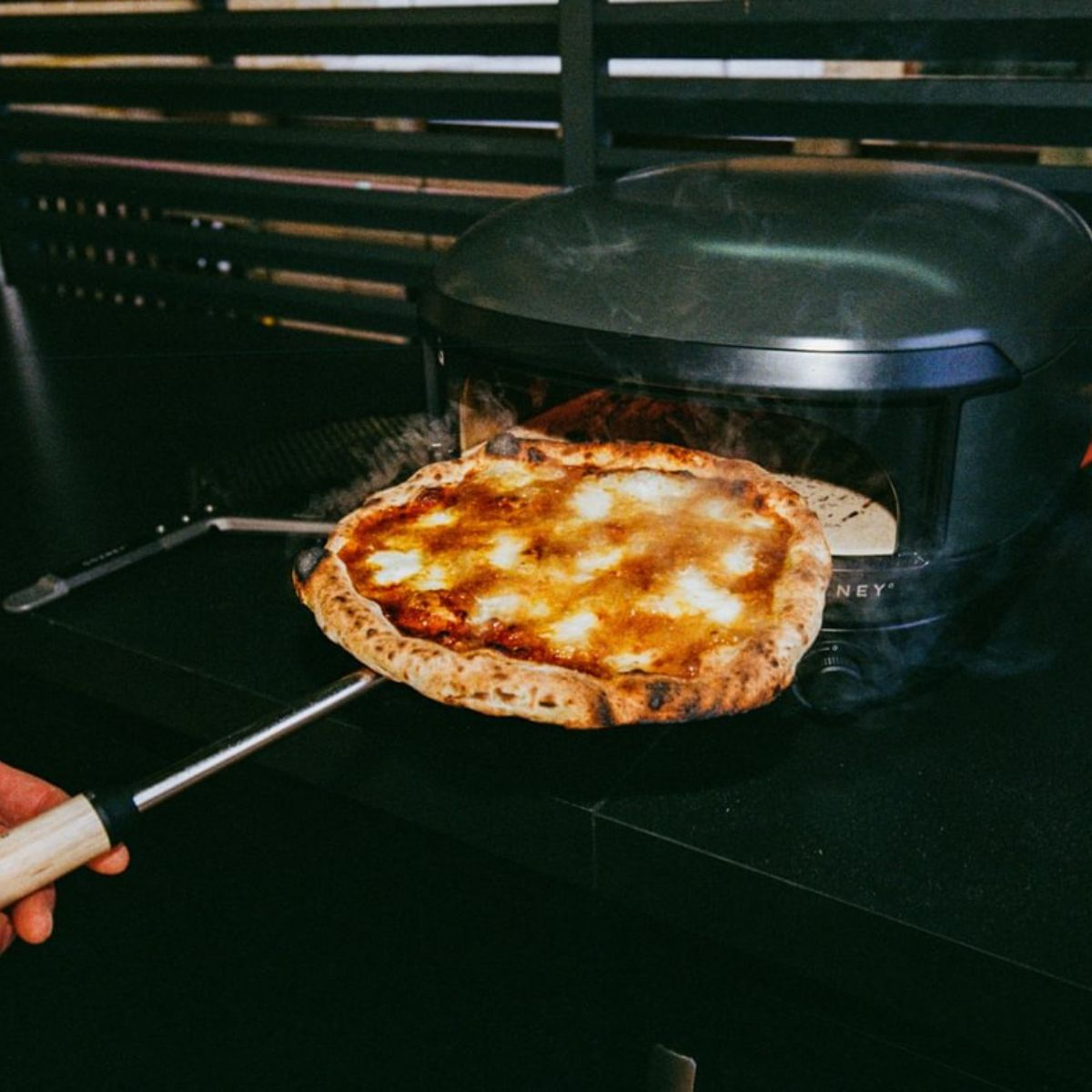 Eine dampfende Pizza wird aus einem Ofen auf einer Pizza-Schaufel genommen.