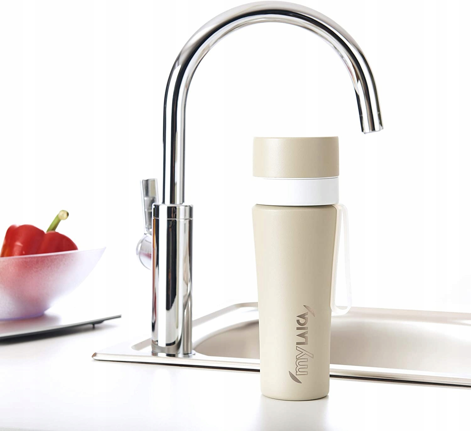 Eine beige Trinkflasche steht neben einem Wasserhahn und einer Schale mit Paprika.