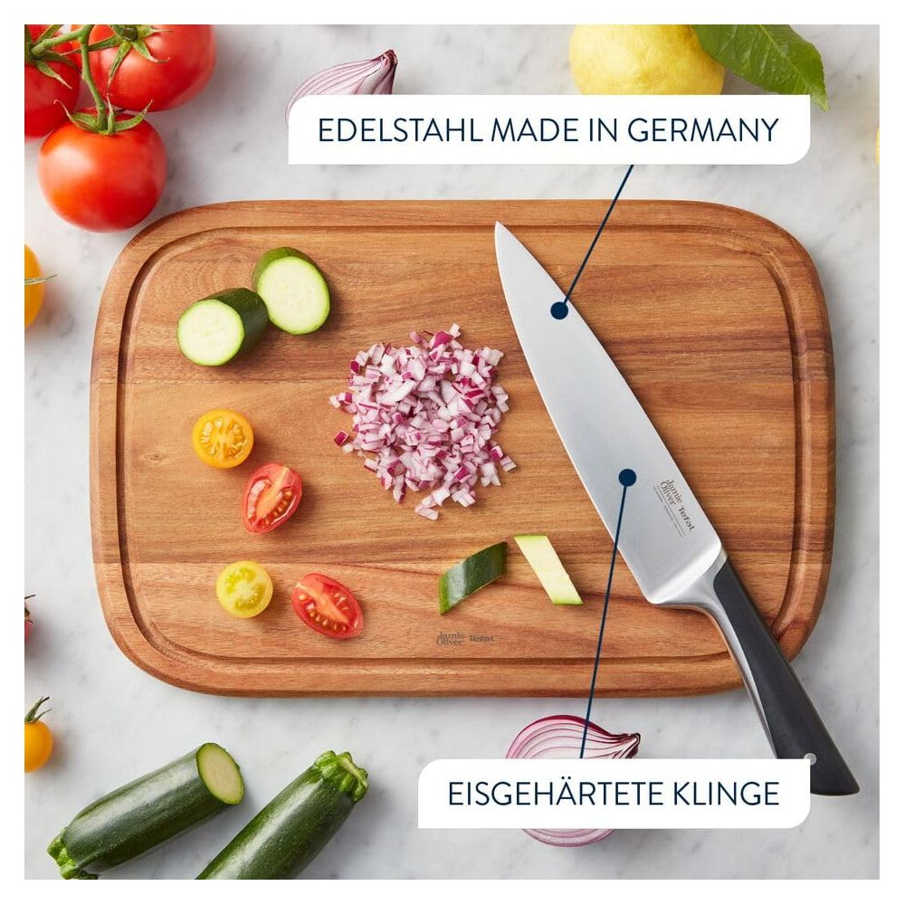 Ein Messer aus Edelstahl liegt auf einem Holzbrett mit gehackten Zwiebeln, Tomaten und Zucchini.
