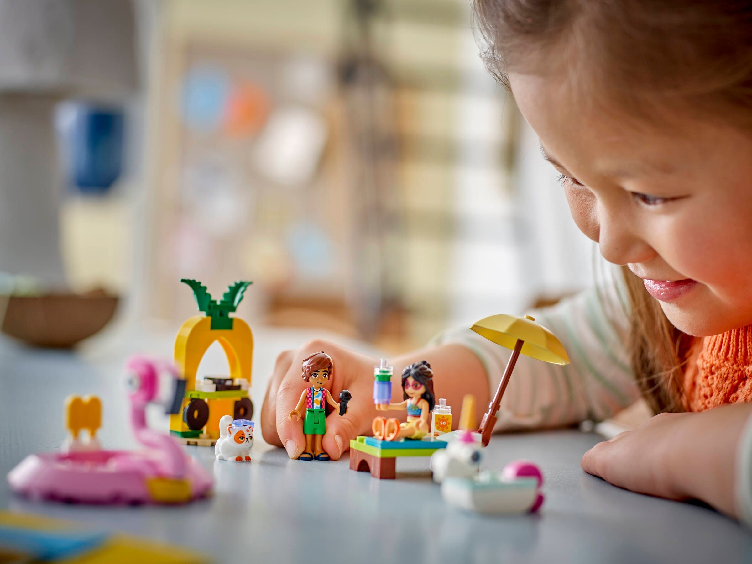 Ein Mädchen spielt mit bunten Lego-Figuren am Strand, darunter ein Flamingo und eine Ananas.