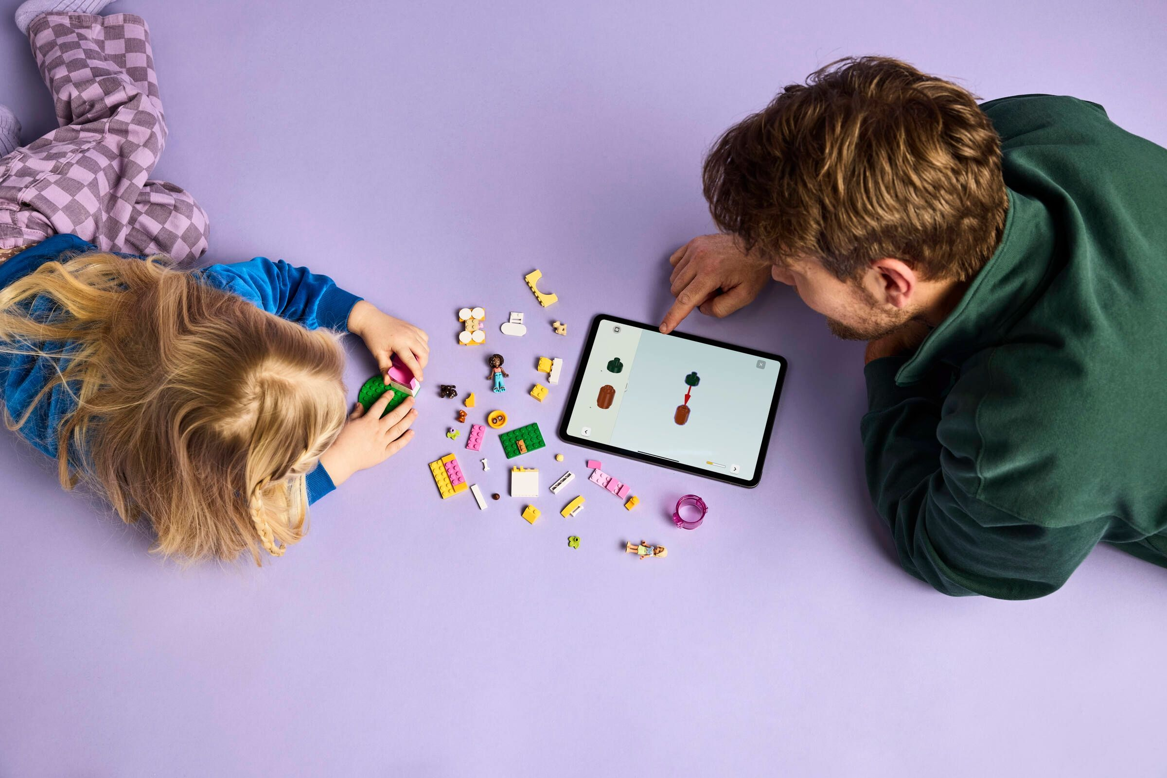 Mann und Kind bauen mit Lego, Anleitung auf Tablet.