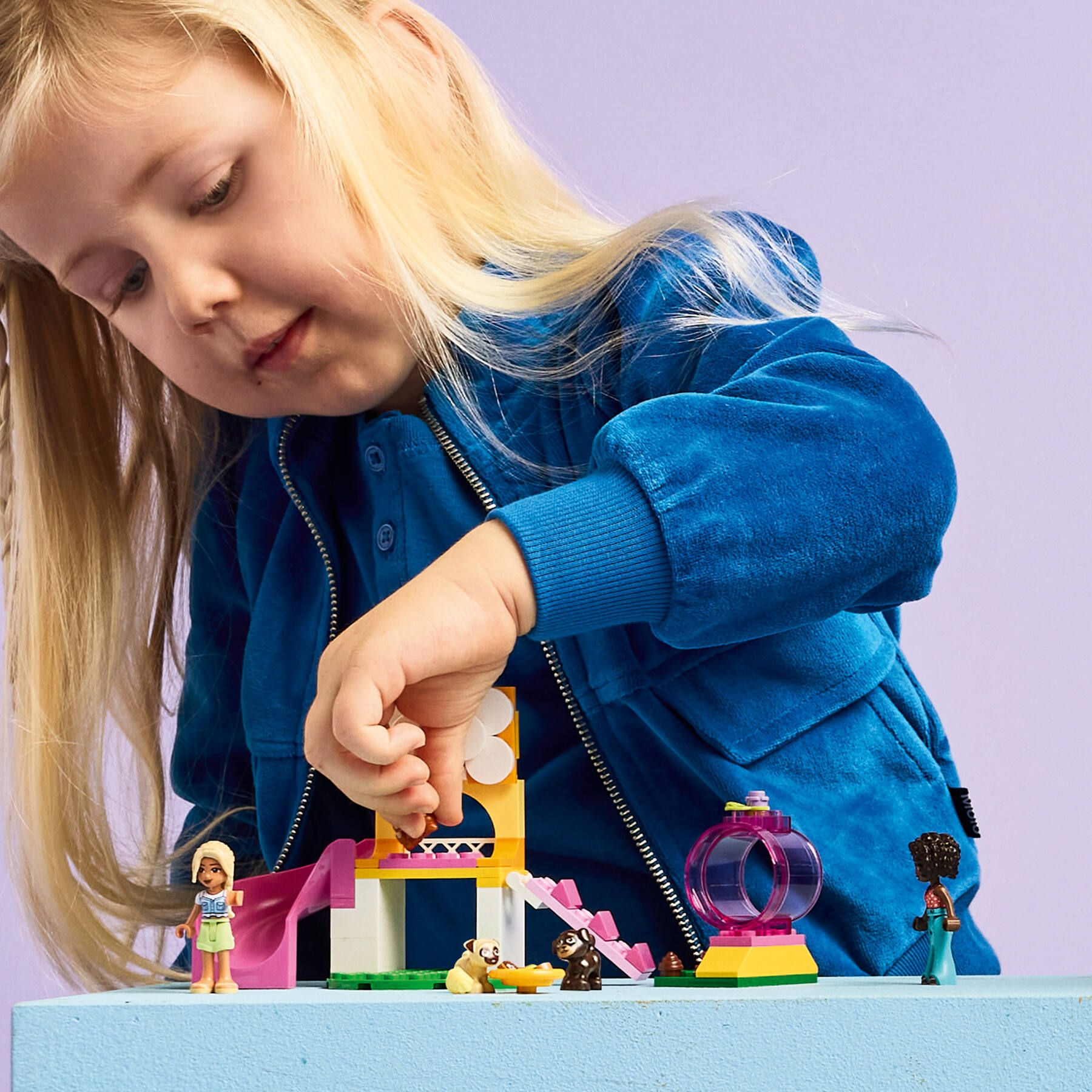 Ein Mädchen spielt mit Lego-Tieren und einer Rutsche auf einem blauen Tisch.