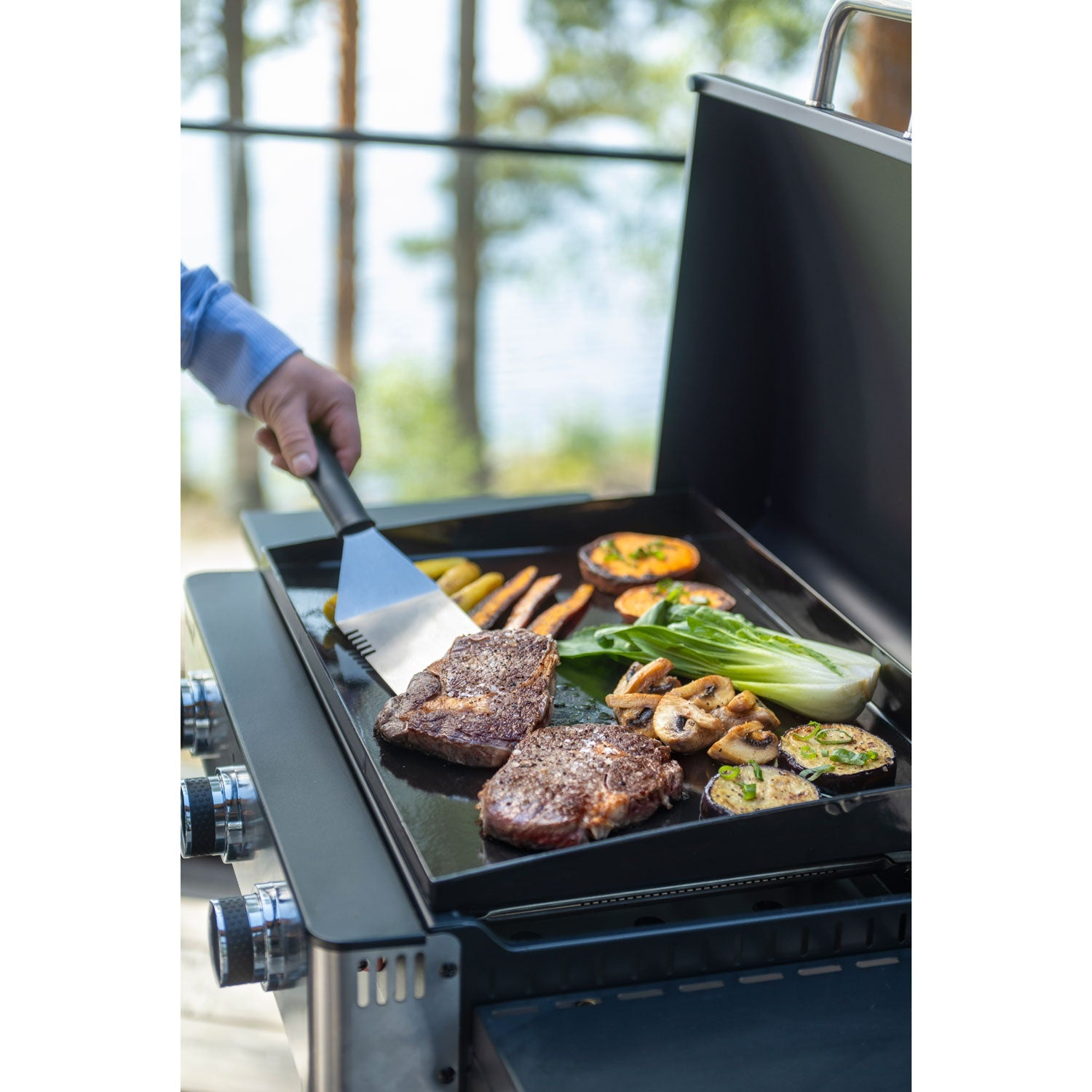 Steaks and vegetables are being grilled outdoors on a flat-top grill.