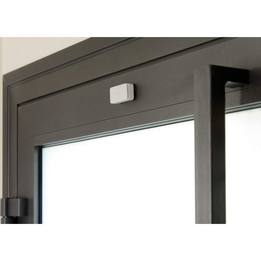 Biały czujnik jest przymocowany do ciemnej ramy okiennej.