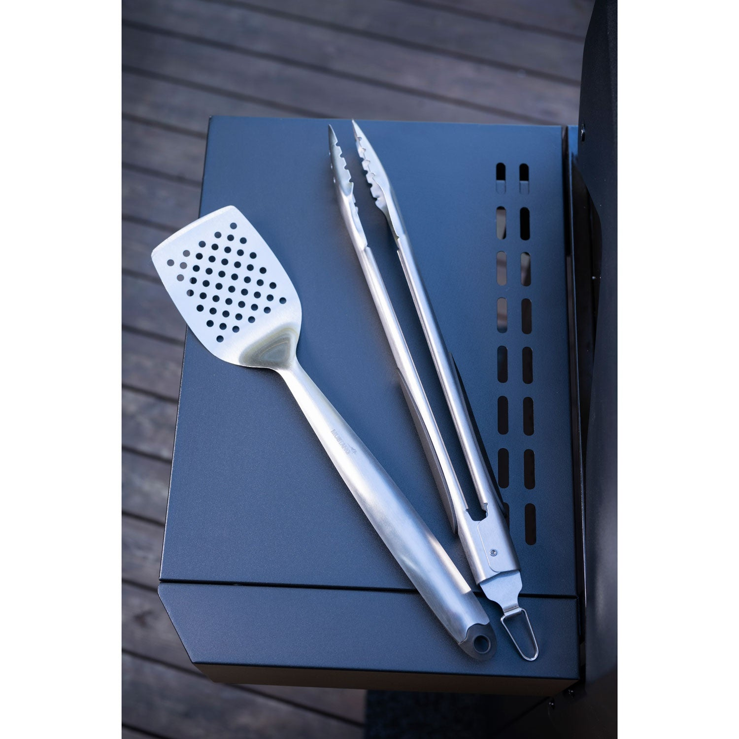Metal grill tongs and spatula on a dark grill.