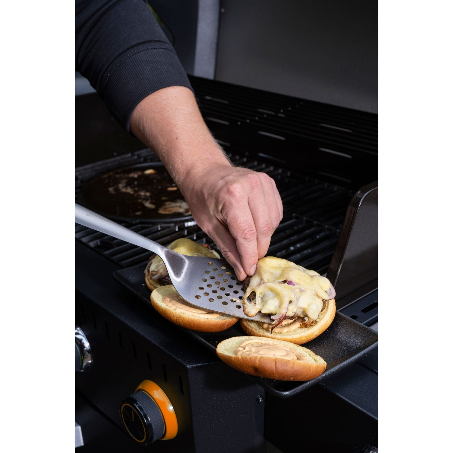 A man places a burger top with melted cheese onto a grill.