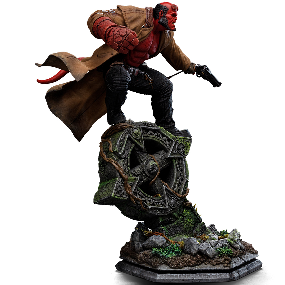 Hellboy mit braunem Mantel und Pistole steht auf einem moosbewachsenen Kreuzsockel.