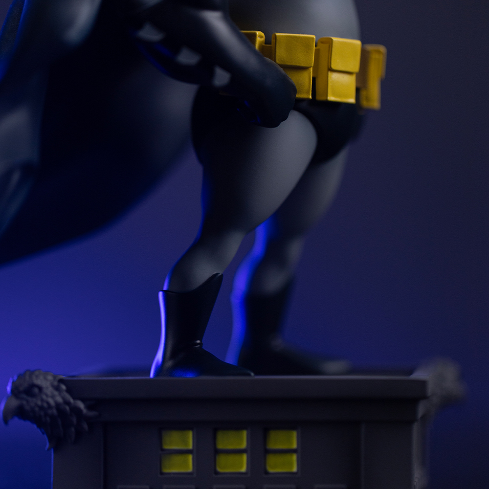 Batman Figur auf Gebäude: schwarzer Umhang, gelber Gürtel, Stiefel.