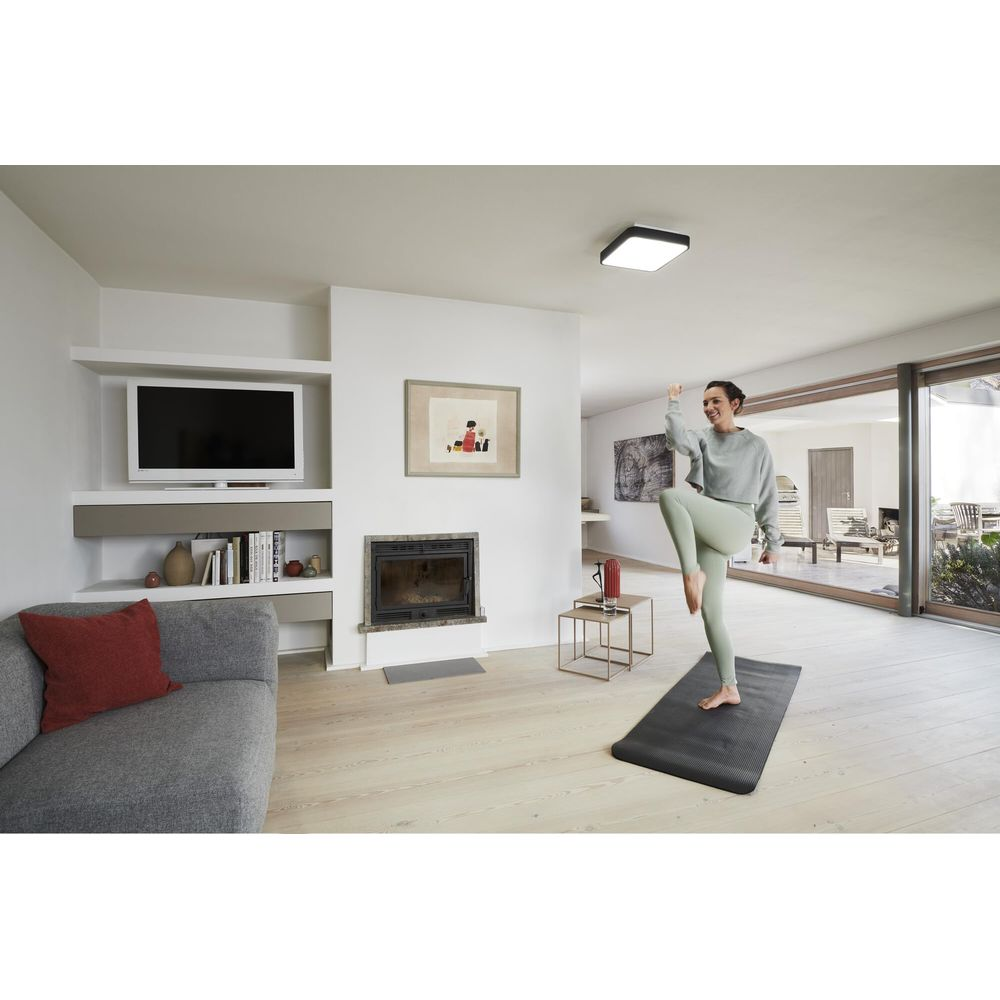 Femme faisant du yoga sur un tapis dans un salon moderne avec cheminée.
