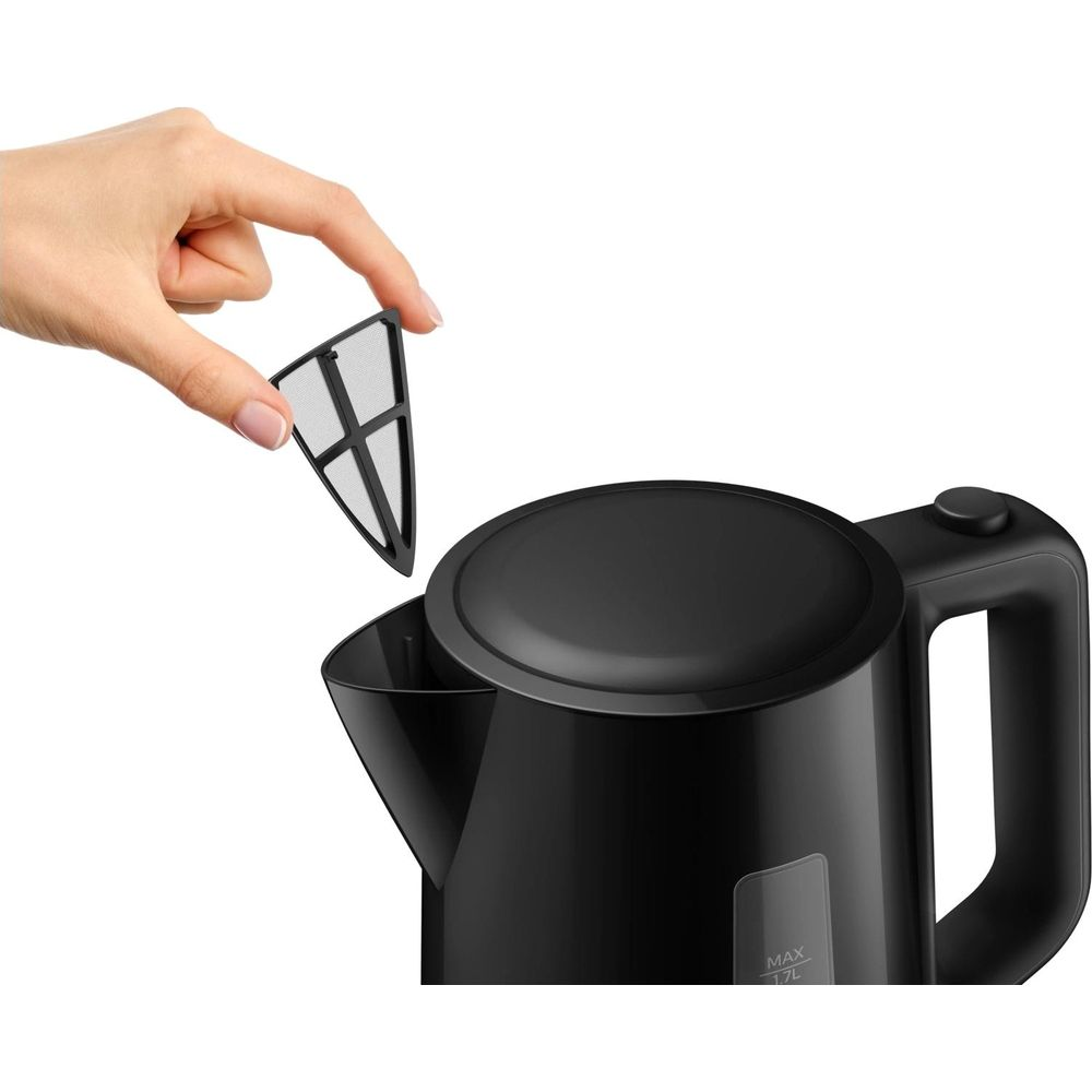 Hand hält schwarzen Teefilter über offenen schwarzen Wasserkocher.