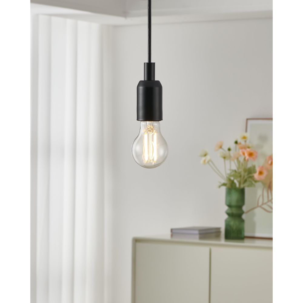 Une suspension noire avec une ampoule Edison est suspendue au-dessus d'une commode blanche.