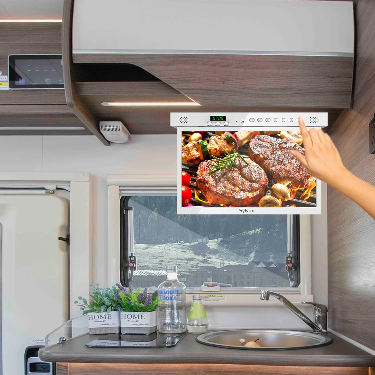 Mano toca pantalla con filetes y verduras a la parrilla en cocina de autocaravana.