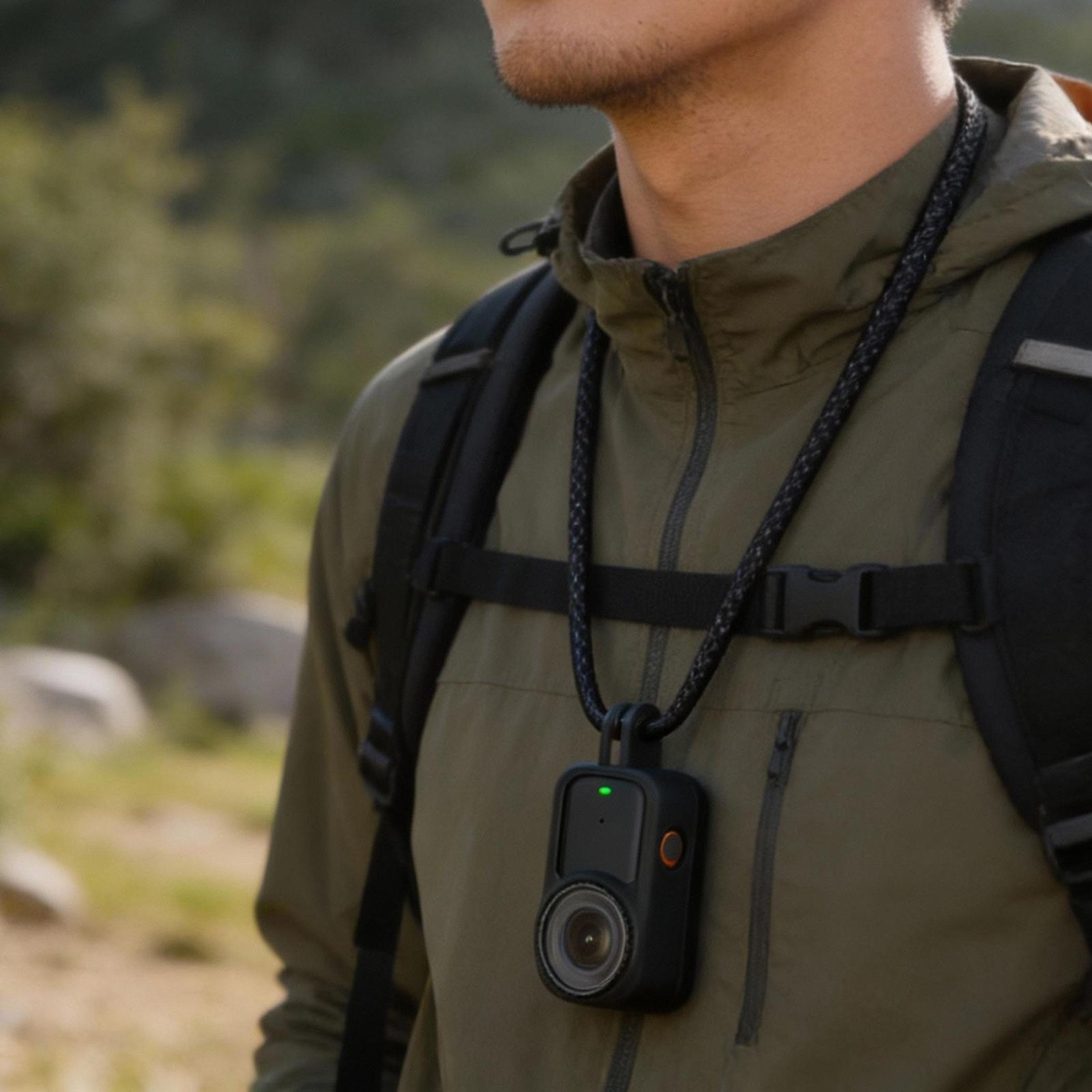 Ein Mann mit Rucksack trägt eine Kamera um den Hals. Grüne und braune Kleidung.