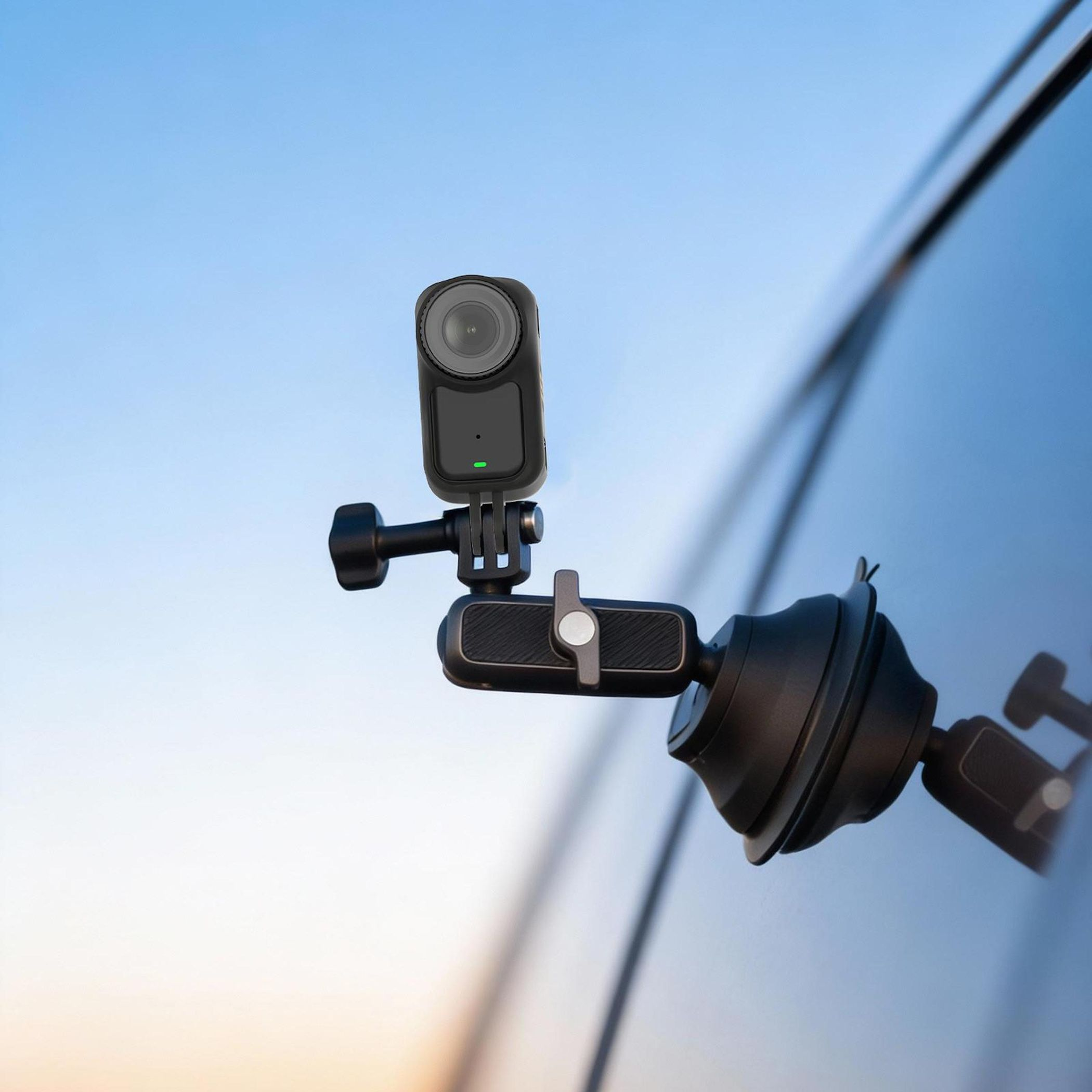 Action-Kamera mit Saugnapfhalterung an einer Autoscheibe vor blauem Himmel.
