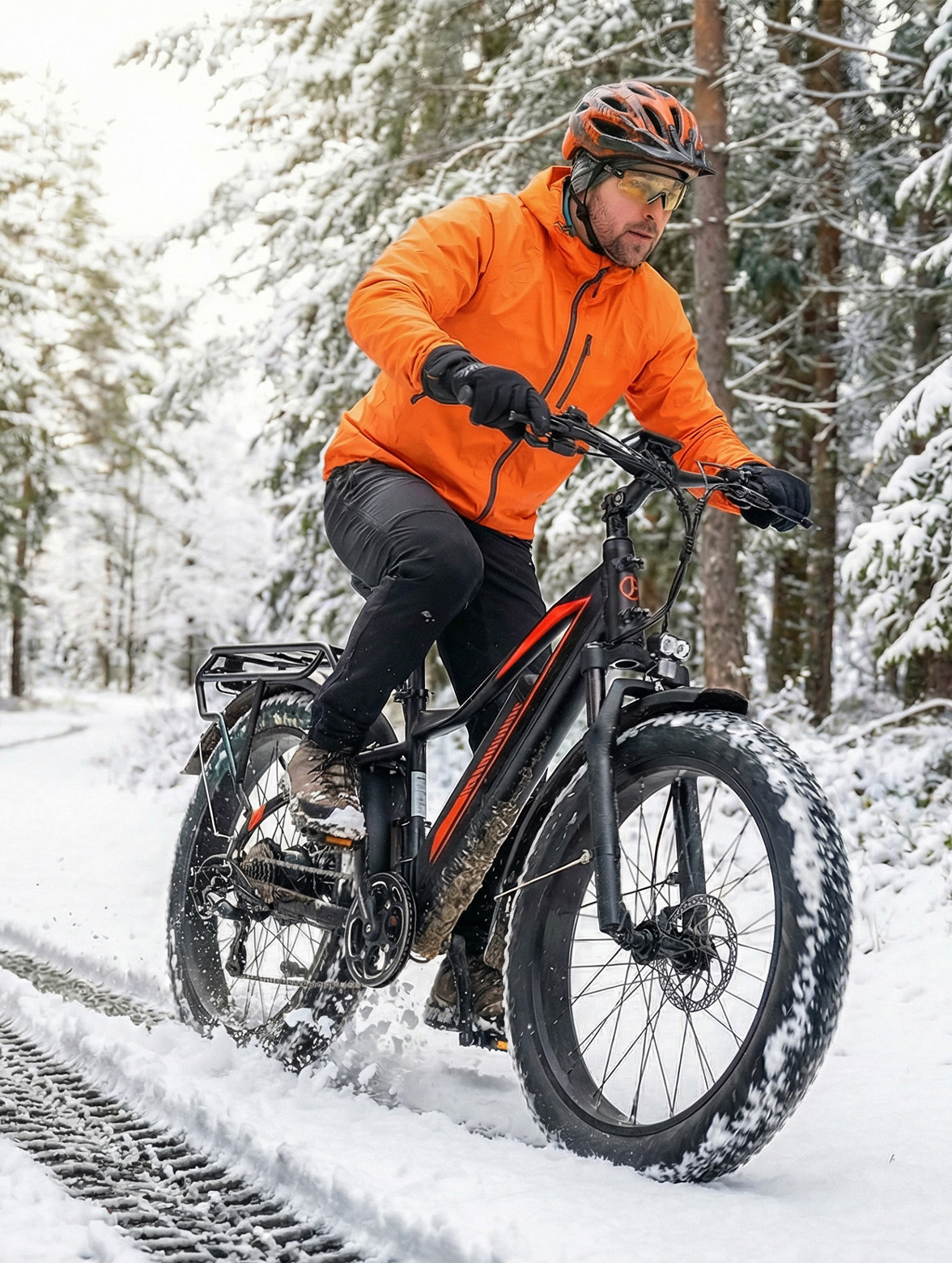 Mann fährt Fatbike im verschneiten Wald. Orange Jacke, Helm, Brille.