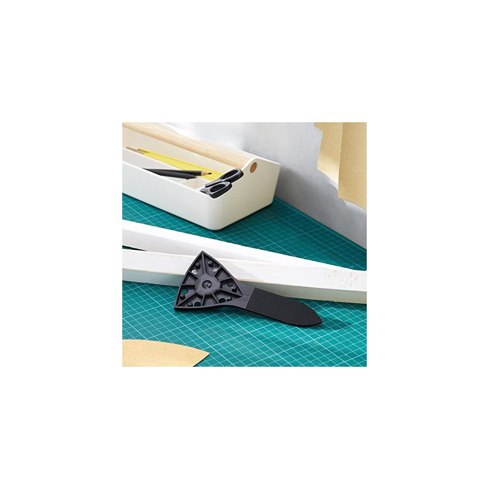 Plateau à outils avec ciseaux et stylos sur un tapis de découpe, à côté d'un grattoir triangulaire.