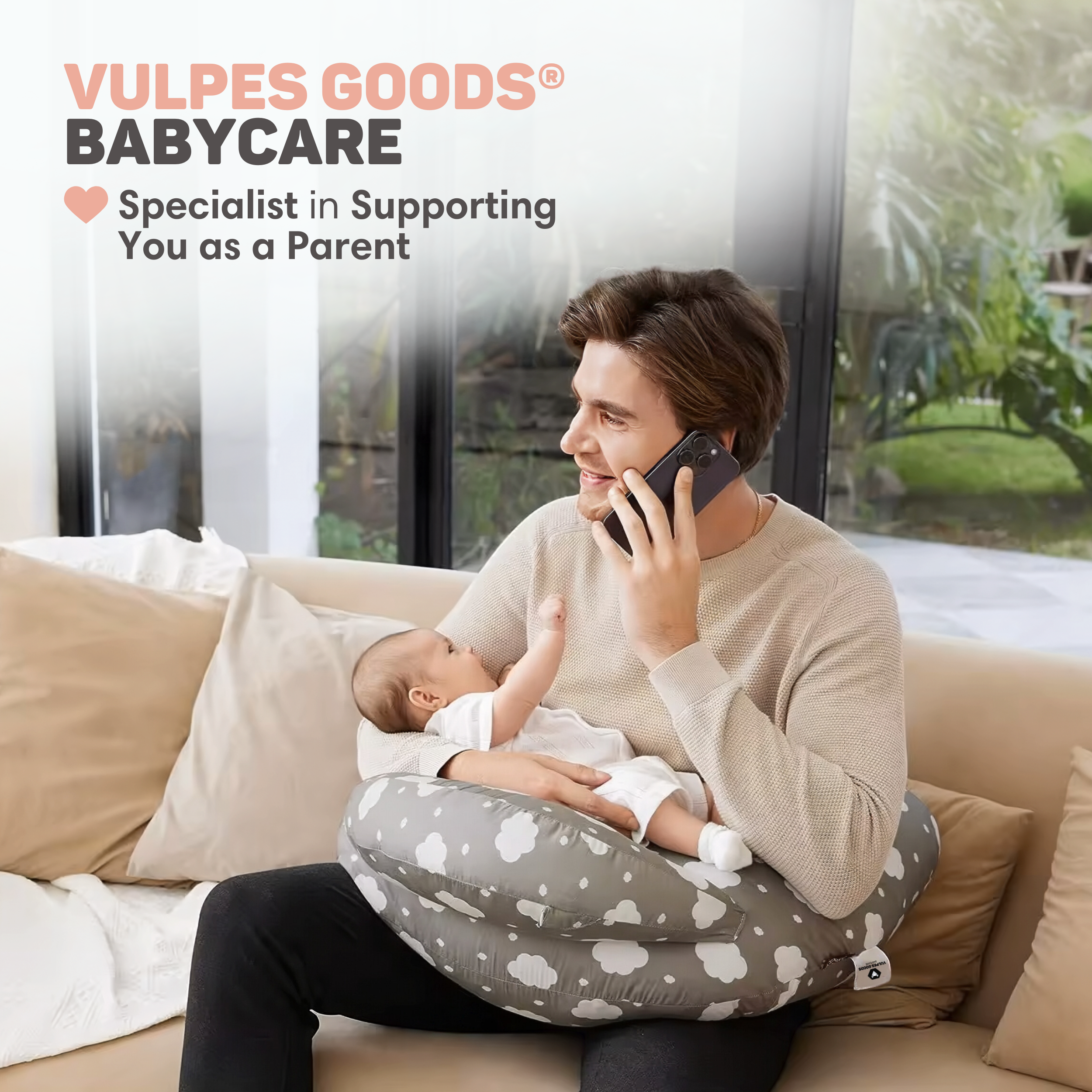Een man aan de telefoon houdt een baby op een voedingskussen met wolkjes.