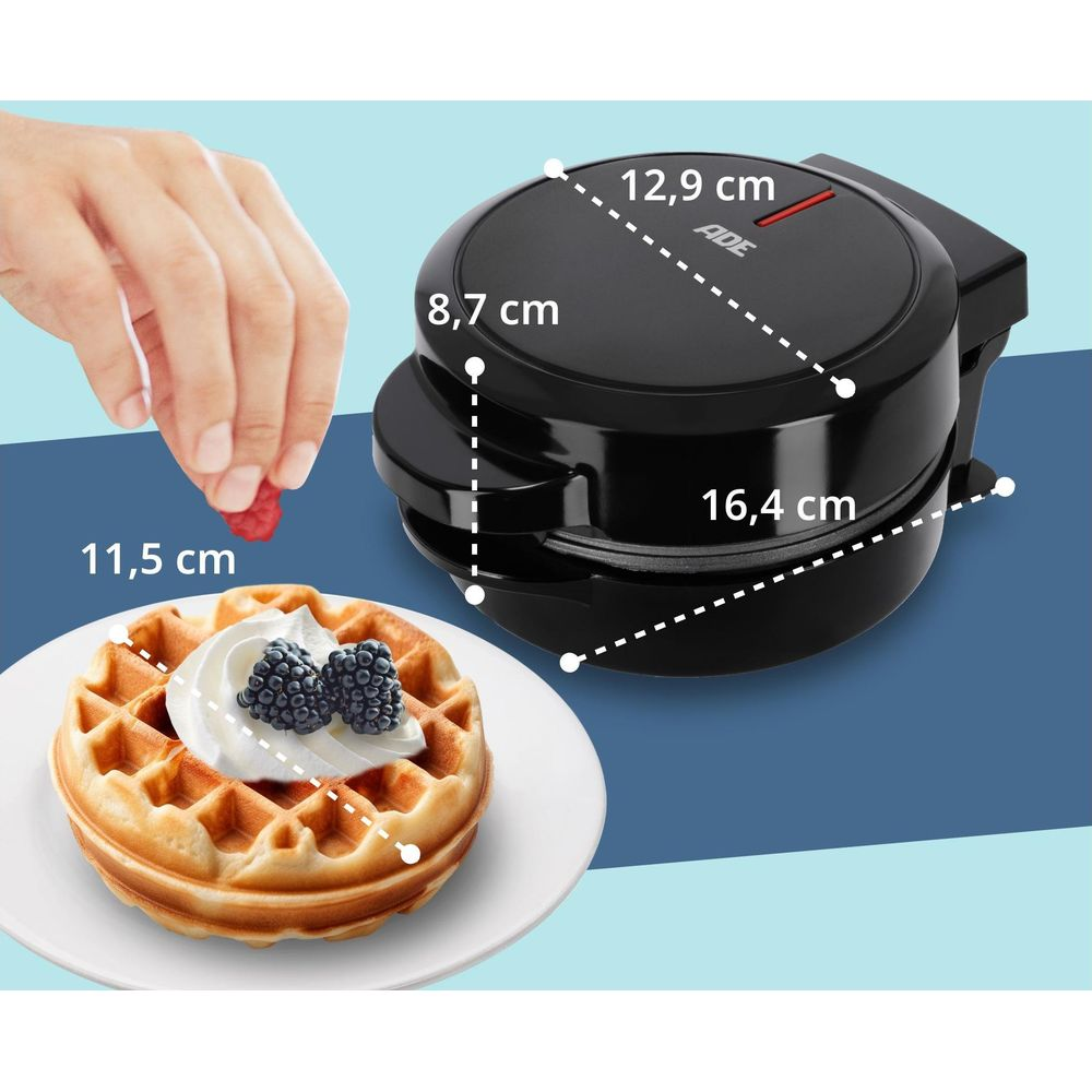 Okrągły gofr z bitą śmietaną i jagodami na talerzu obok gofrownicy.