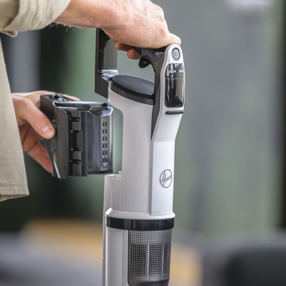 Ręka wyjmuje baterię z białego odkurzacza.