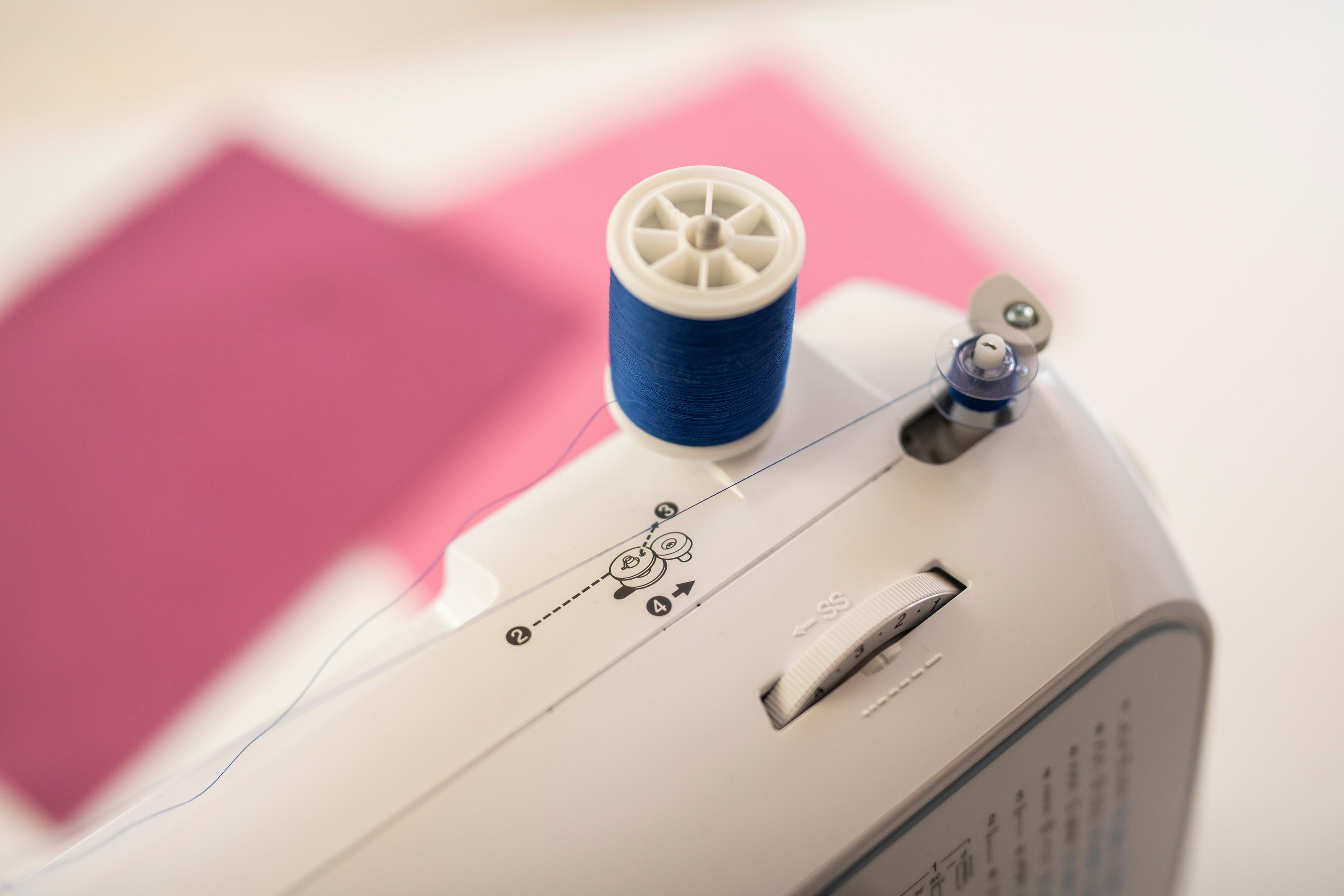 Zbliżenie maszyny do szycia z niebieską szpulą nici i pokrętłem ustawień.