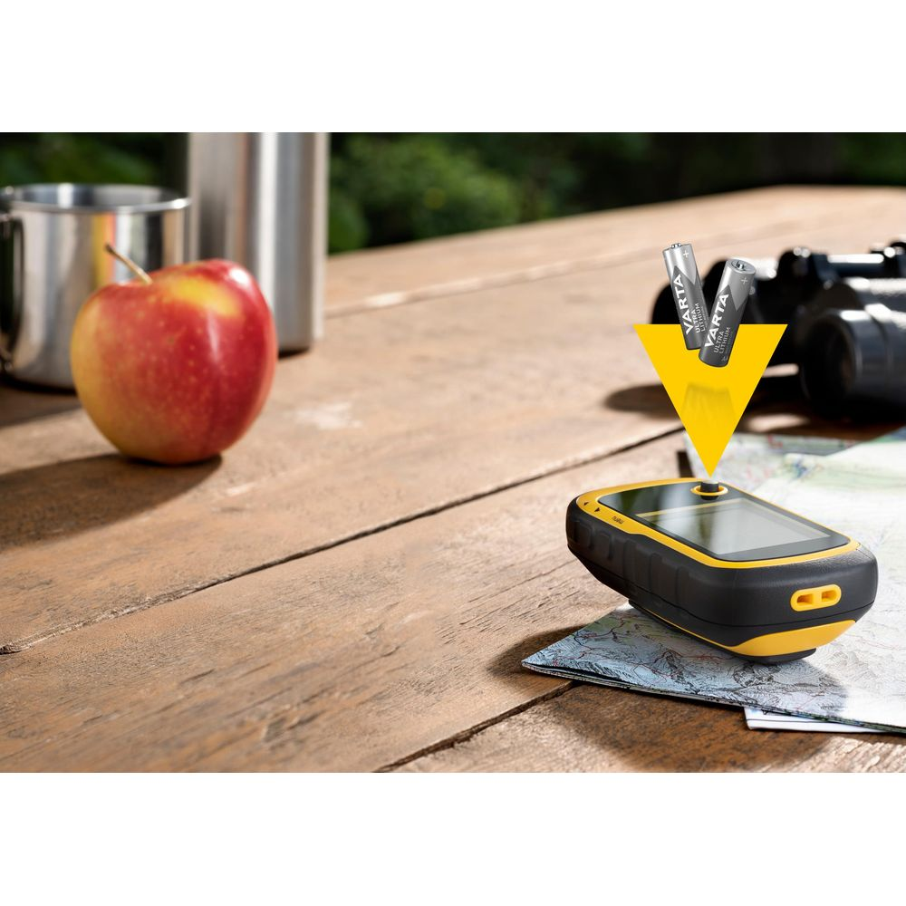 GPS device with batteries, apple, and thermos on a wooden table.