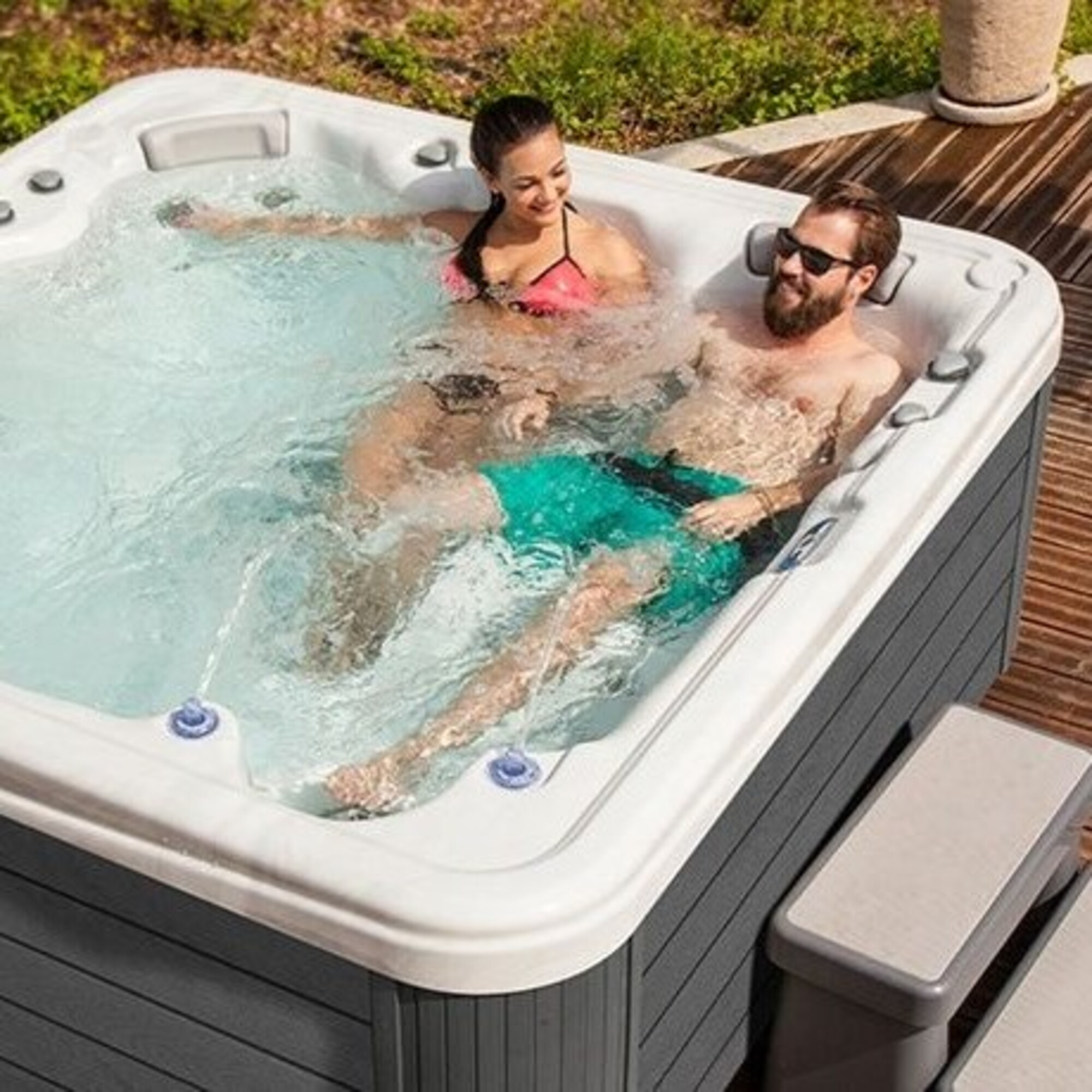 Una pareja se relaja en un jacuzzi exterior rodeado de vegetación.