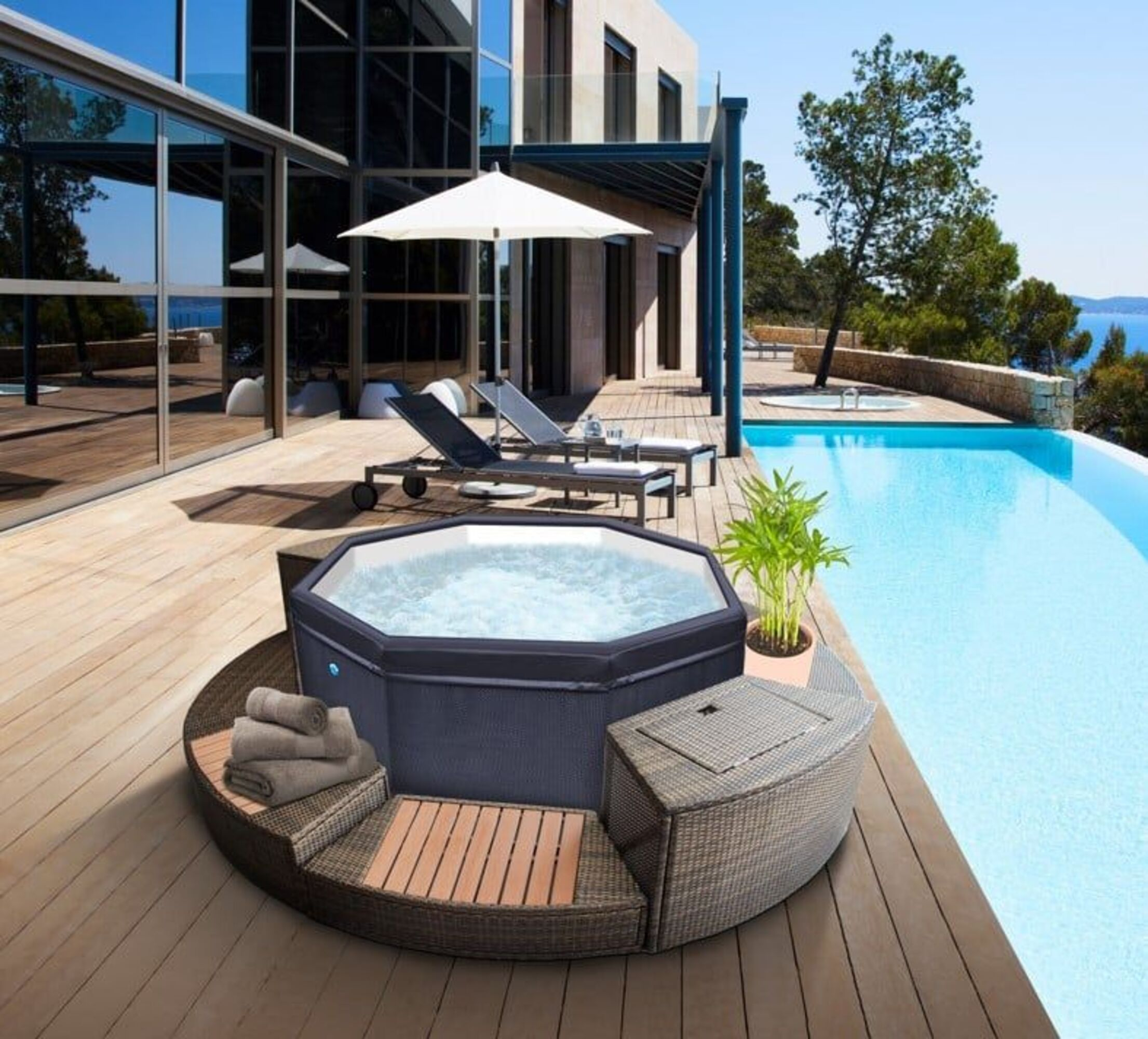 Un jacuzzi inflable en una terraza de madera junto a una piscina con vistas al mar.