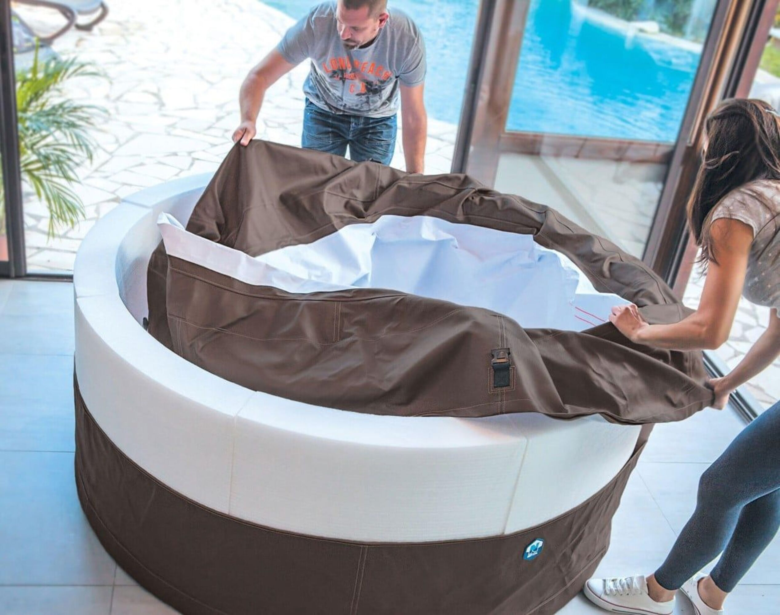 Hombre y mujer colocan cubierta marrón sobre jacuzzi inflable.