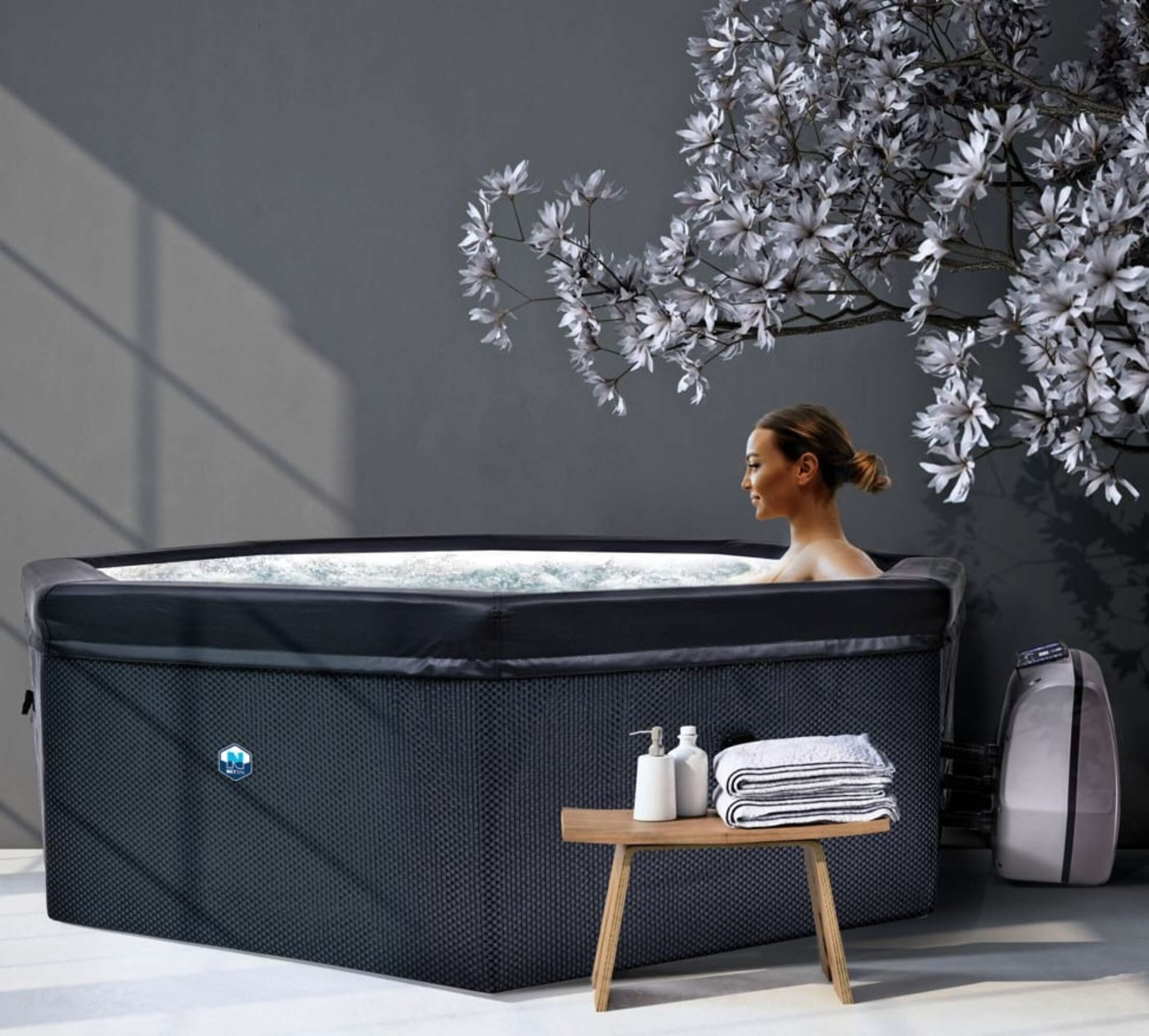Una mujer se relaja en un jacuzzi inflable con flores blancas al fondo.