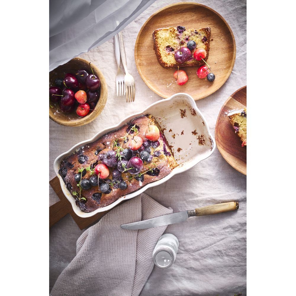 Ein Kuchen mit Kirschen und Blaubeeren in einer weißen Form, daneben eine Schüssel Kirschen.