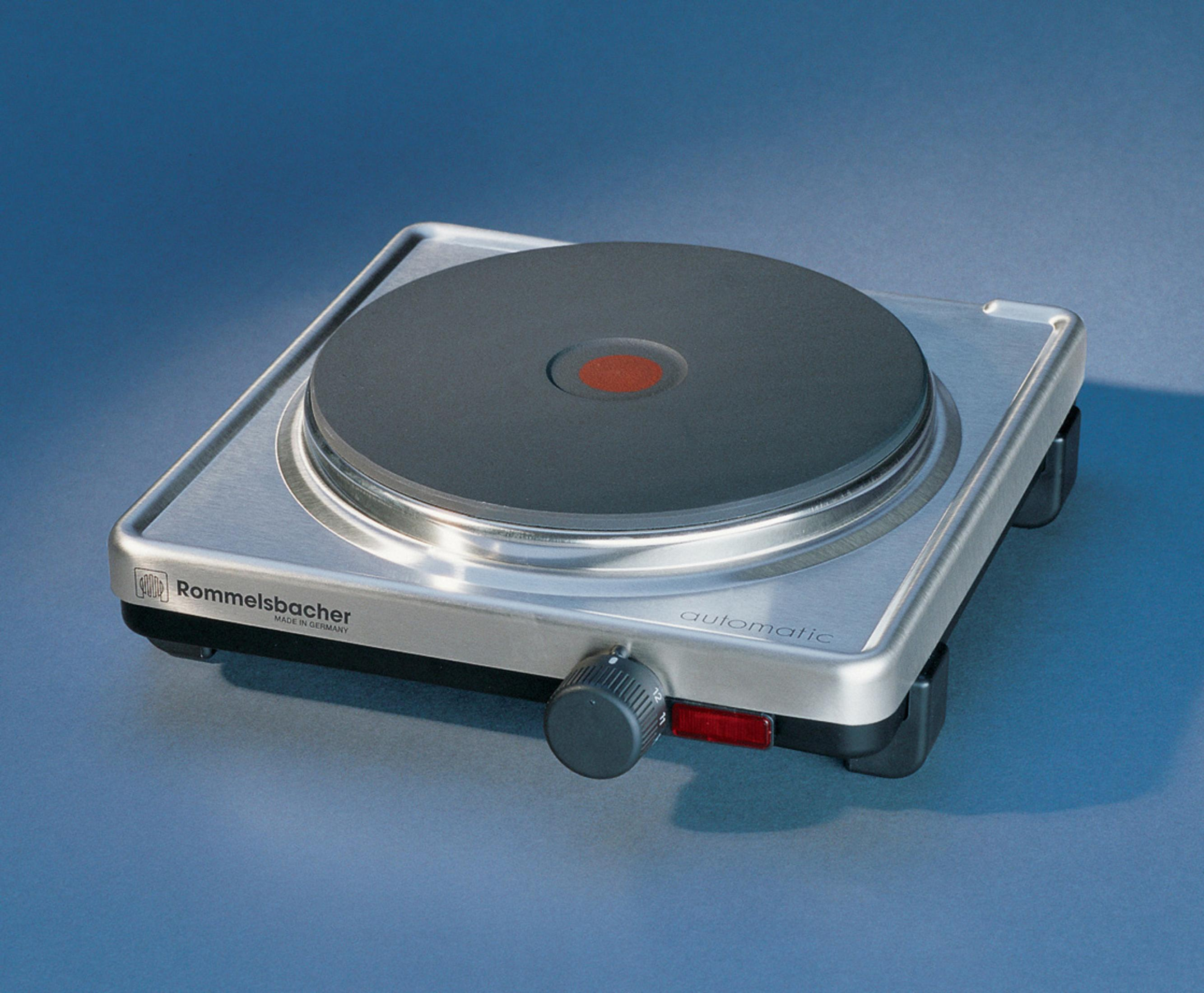 Srebrna kuchenka elektryczna z czarną płytą i czerwonym środkiem na niebieskiej powierzchni.