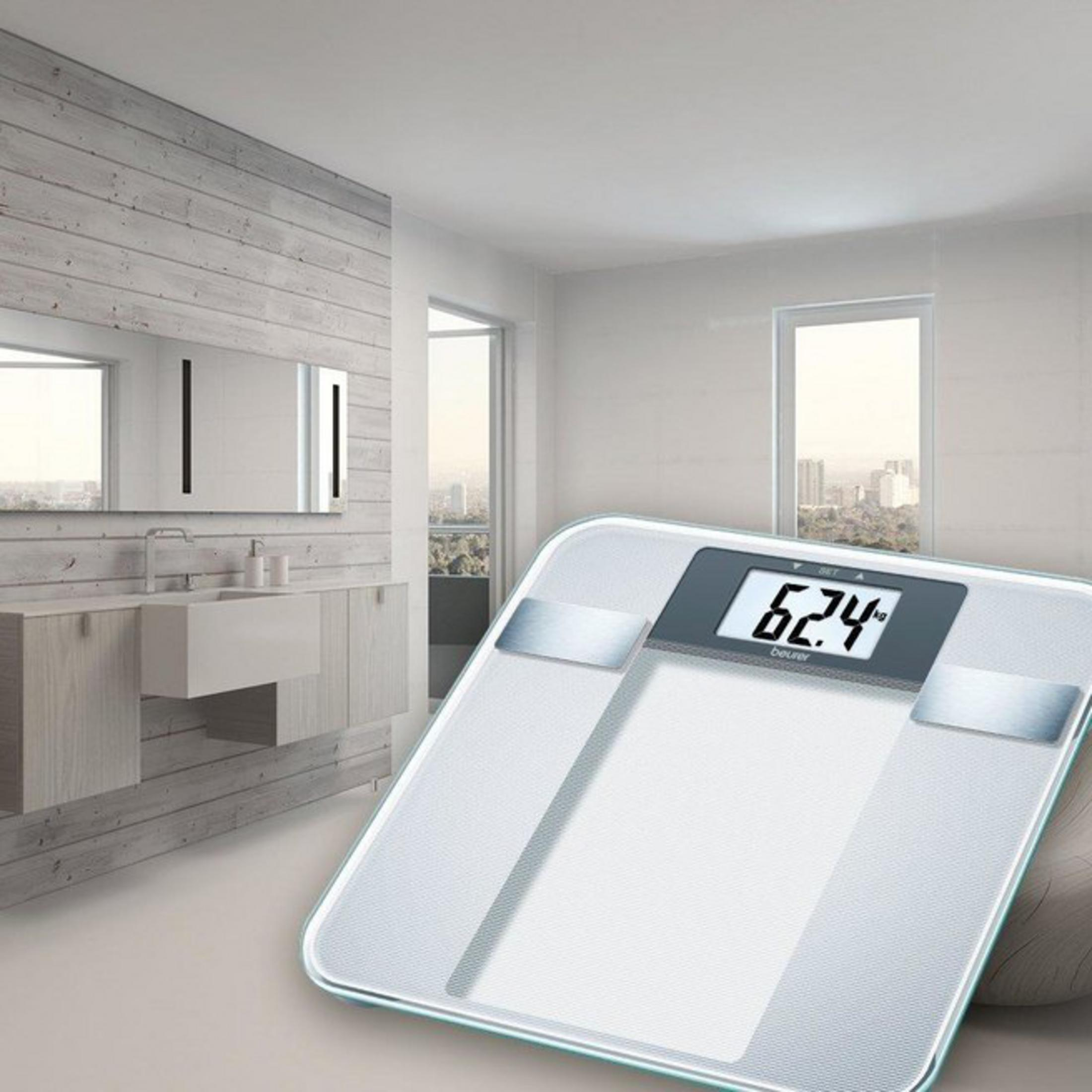 Digitale Personenwaage zeigt 62,4 kg an, mit einem Badezimmer im Hintergrund.